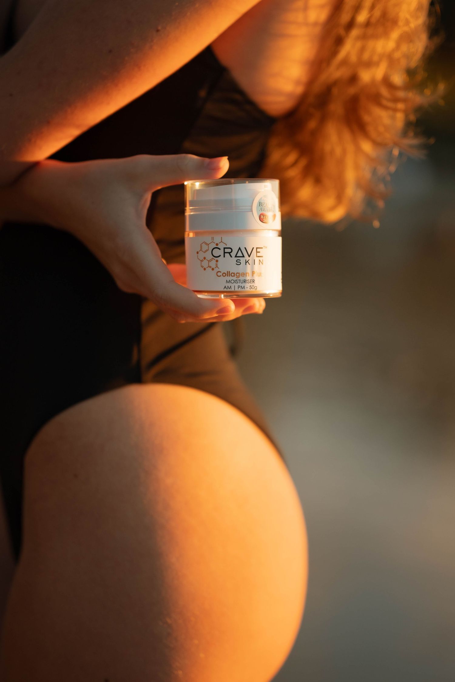 Woman holding Crave Skin Collagen moisturizer jar in golden sunset light.