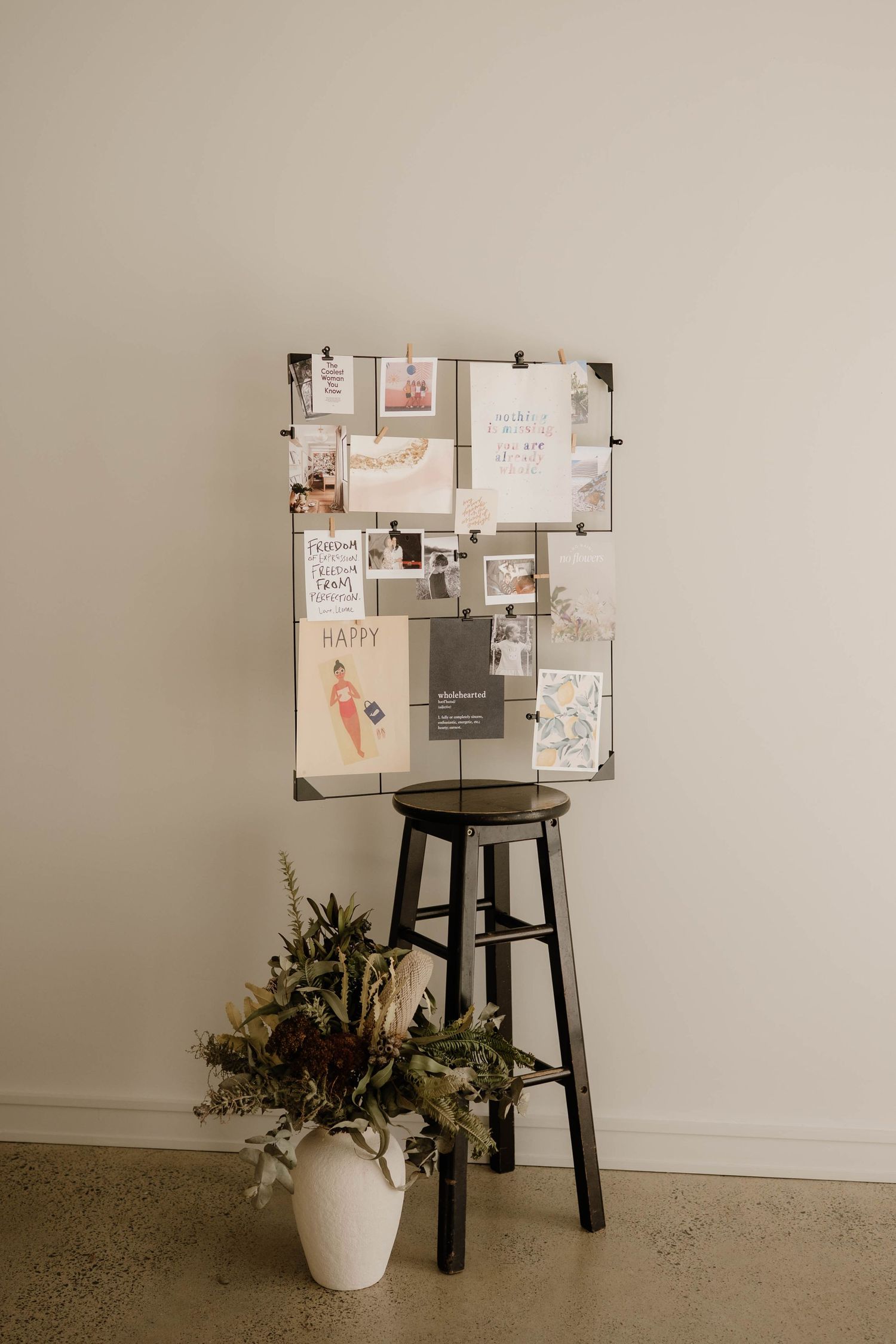 Decorative mood board with photos and cards displayed on metal grid above black stool.