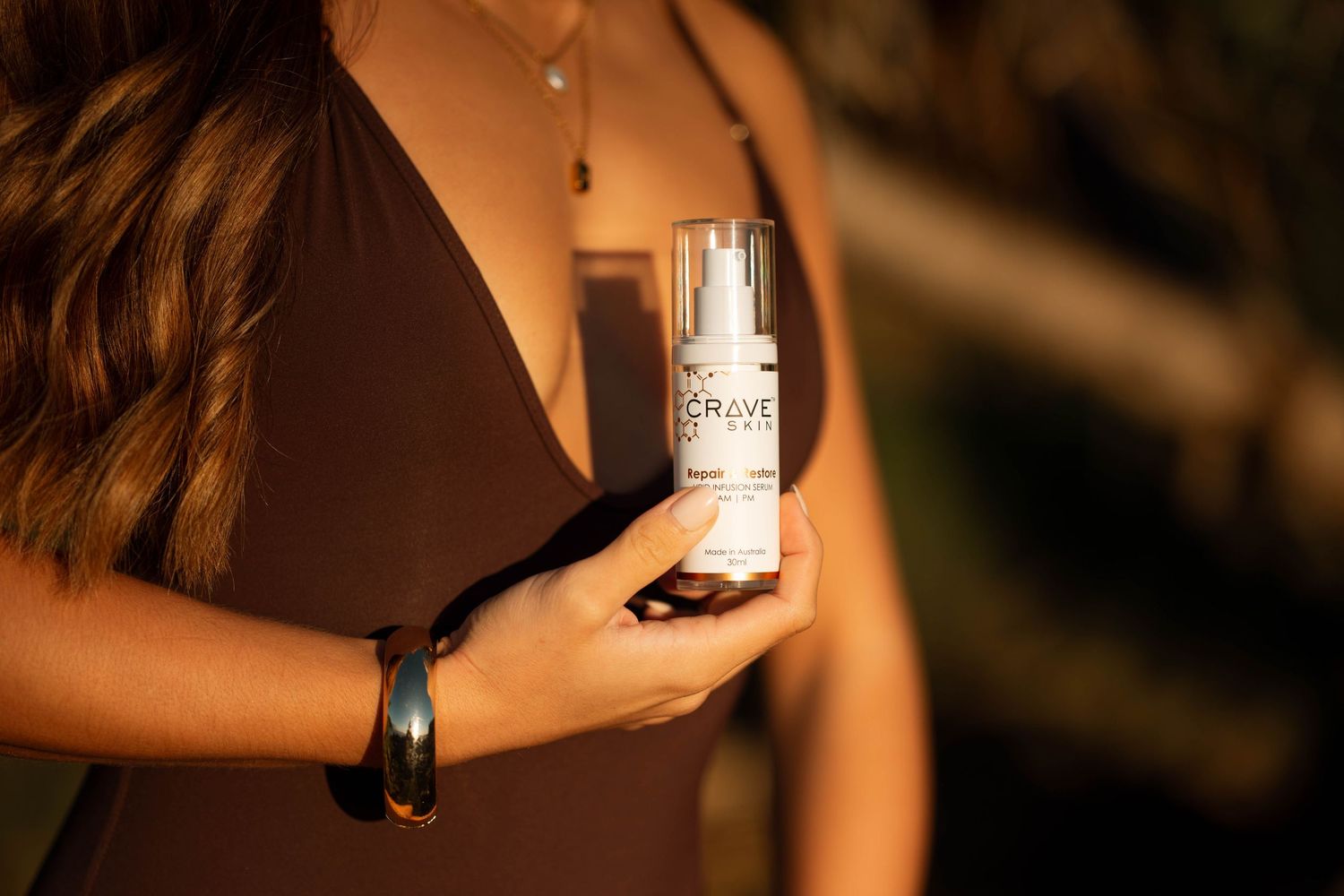 Close-up of woman holding Crave branded skincare spray bottle in warm golden sunlight.