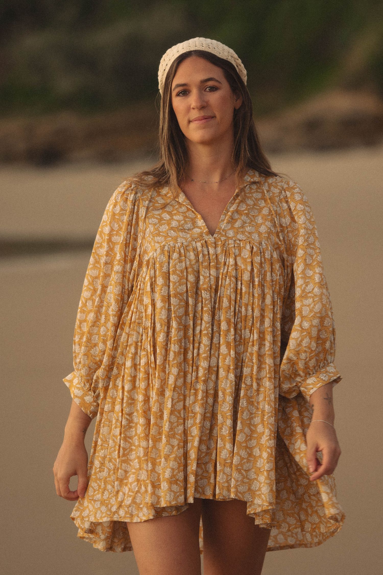 Woman in yellow floral mini dress and headband walking on beach.