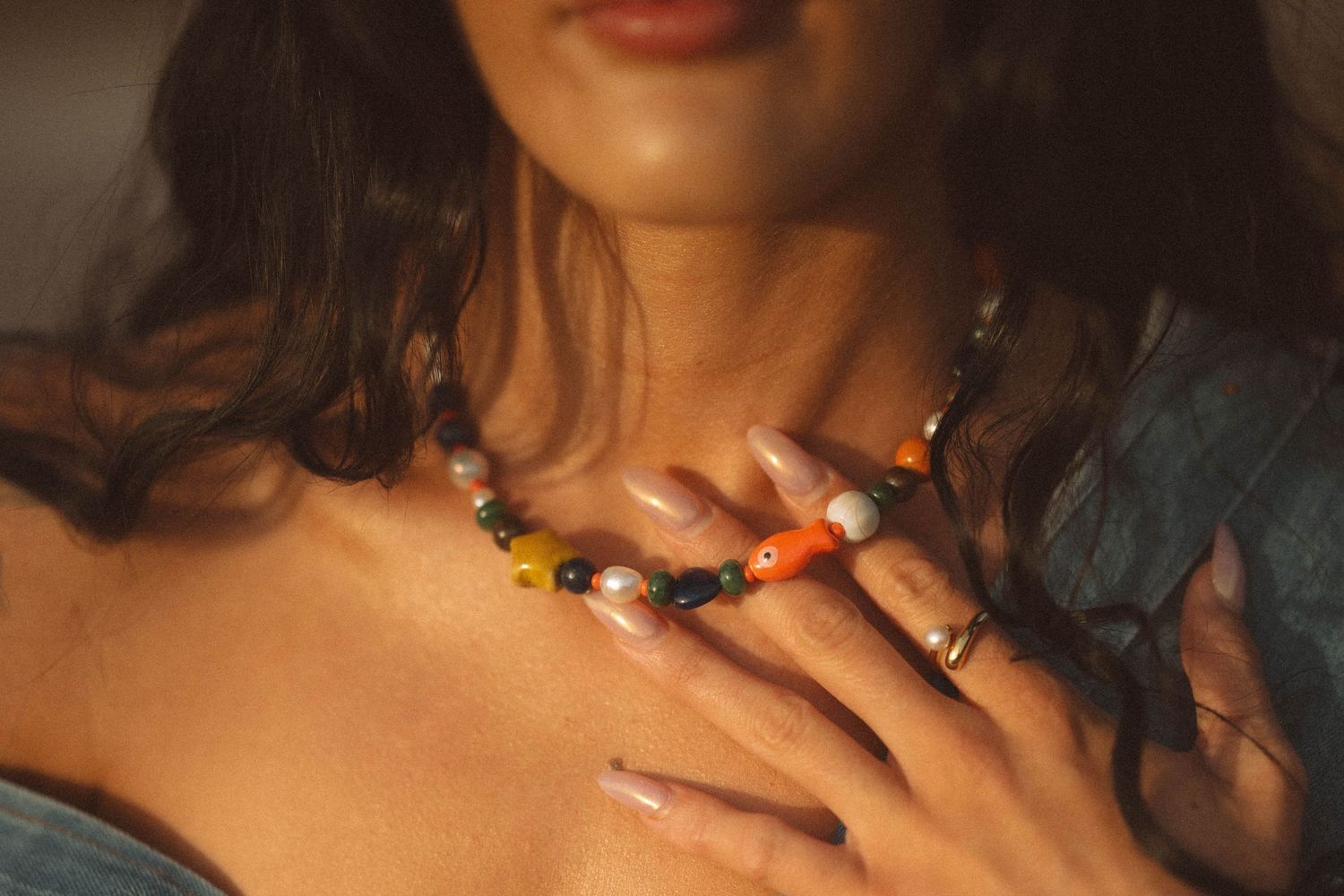 Woman wearing colorful beaded necklace and rings, gently touching her chest, adorned with boho jewelry.