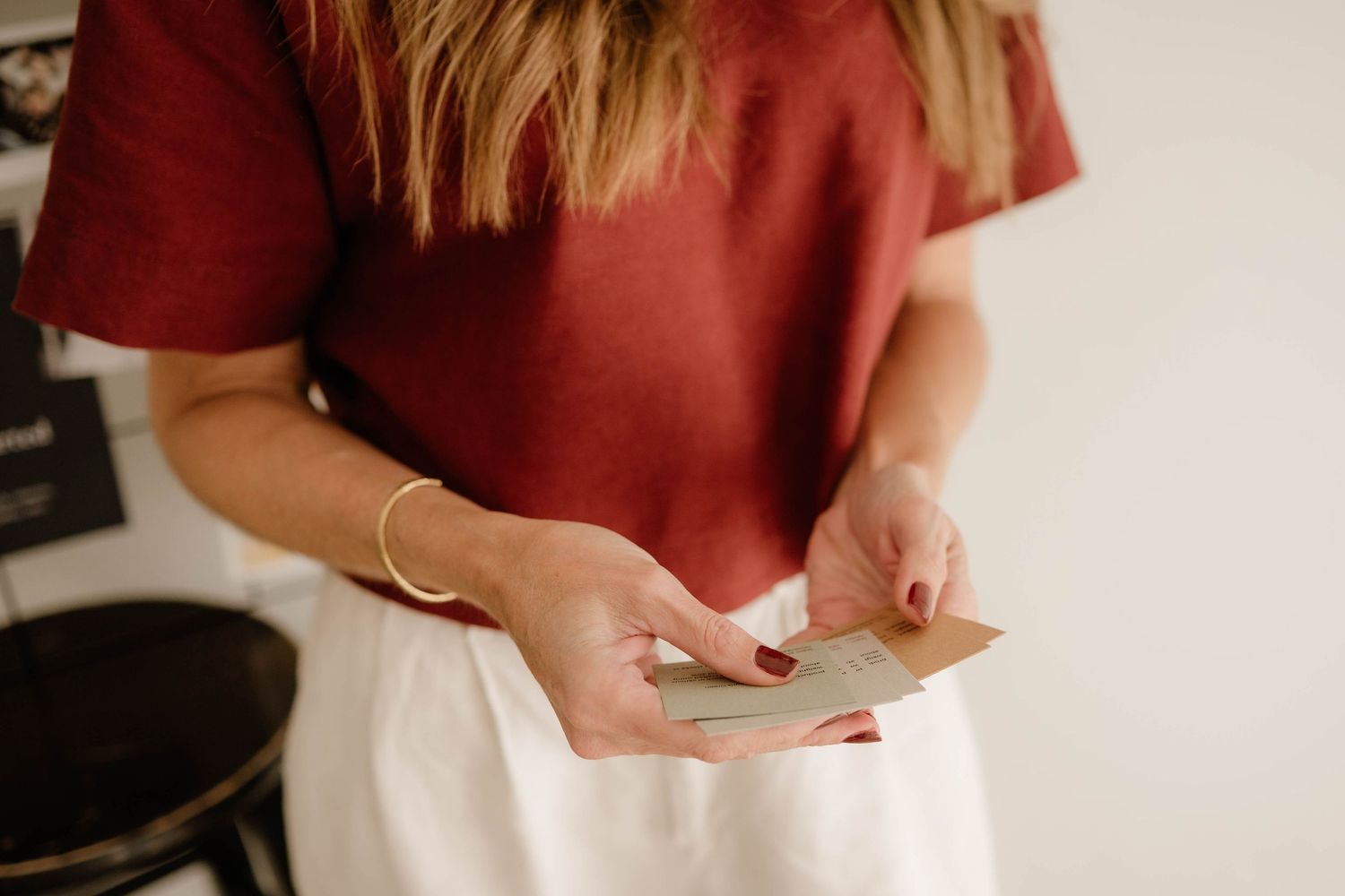 Close-up of woman in red top holding small cards with gold bracelet on wrist.