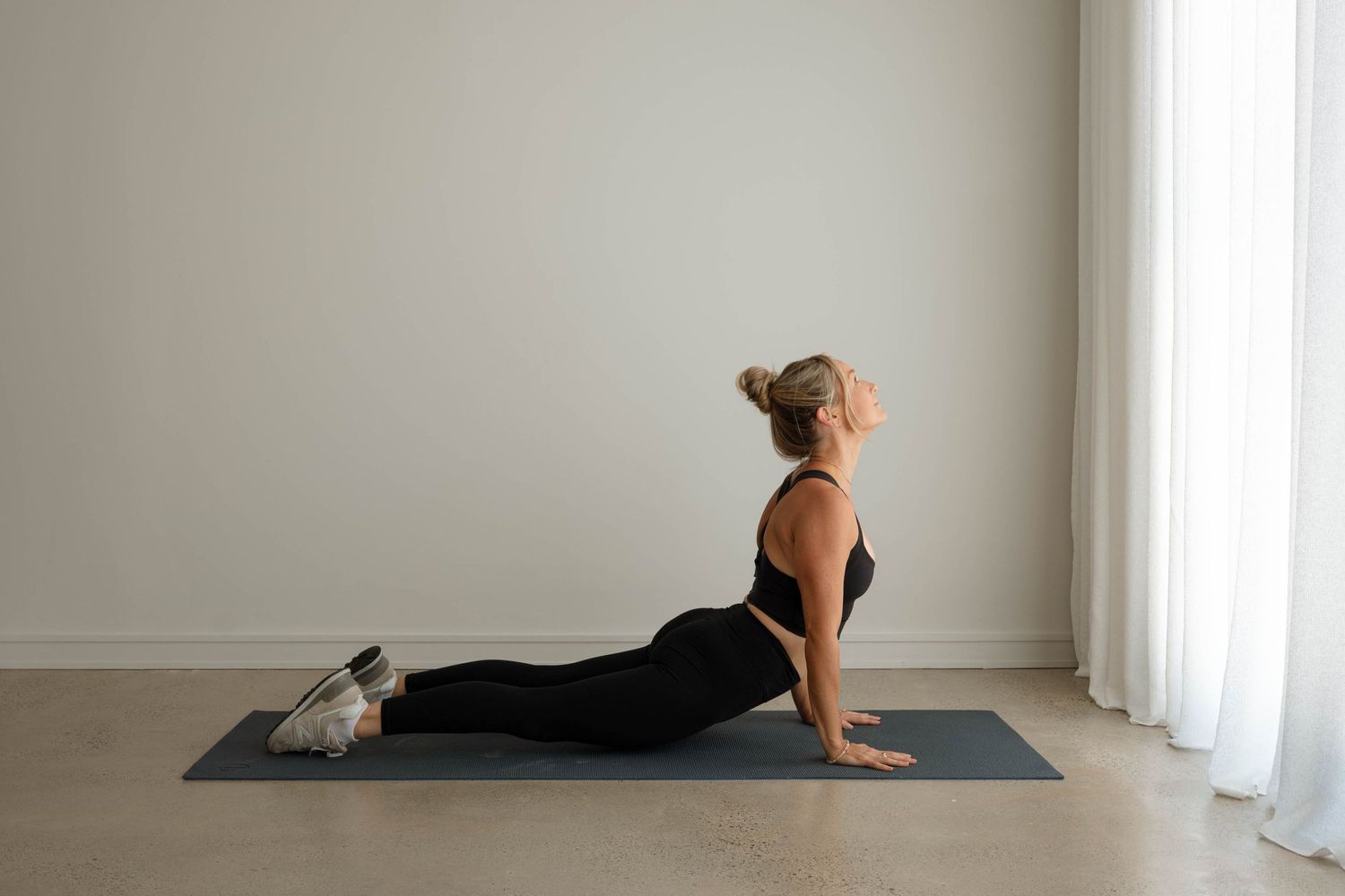 Woman in black activewear performing cobra pose on a yoga mat indoors.