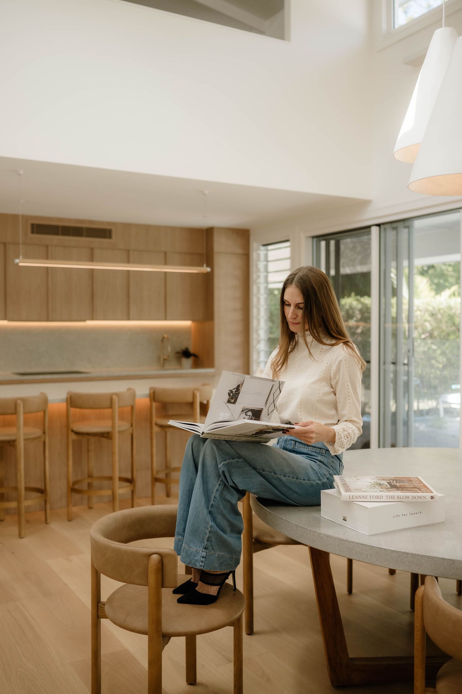 Woman browsing an interior design magazine at a round dining table in a modern home.