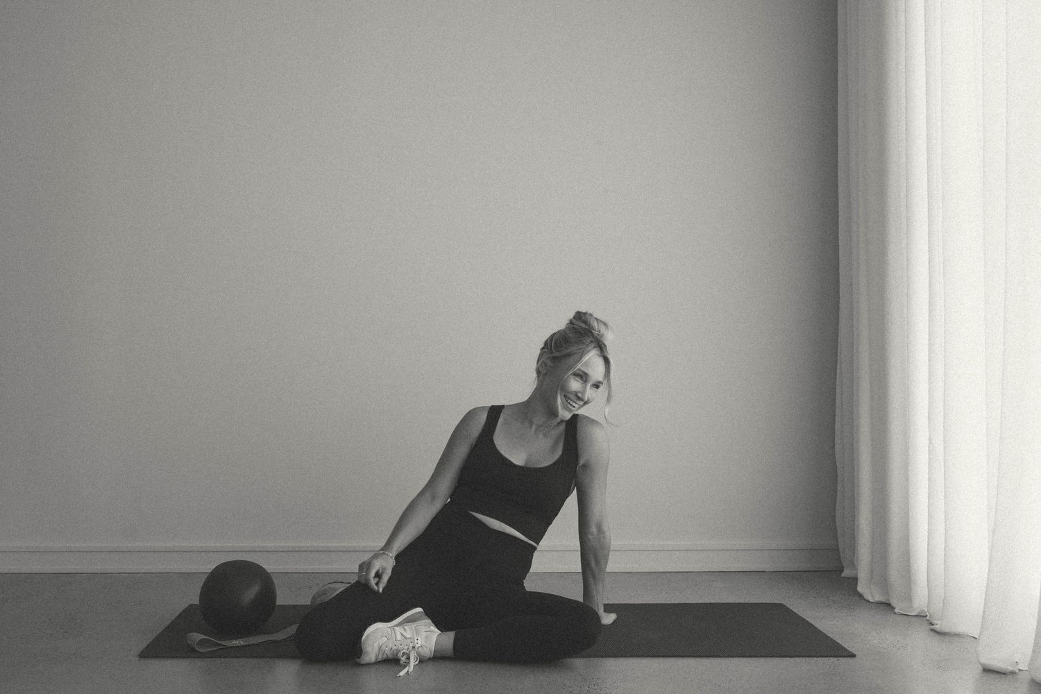Black and white photo of woman in activewear relaxing on yoga mat with exercise ball.