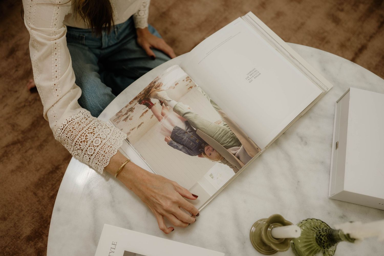 Woman opening a white photo album on a marble coffee table in a cozy living room.
