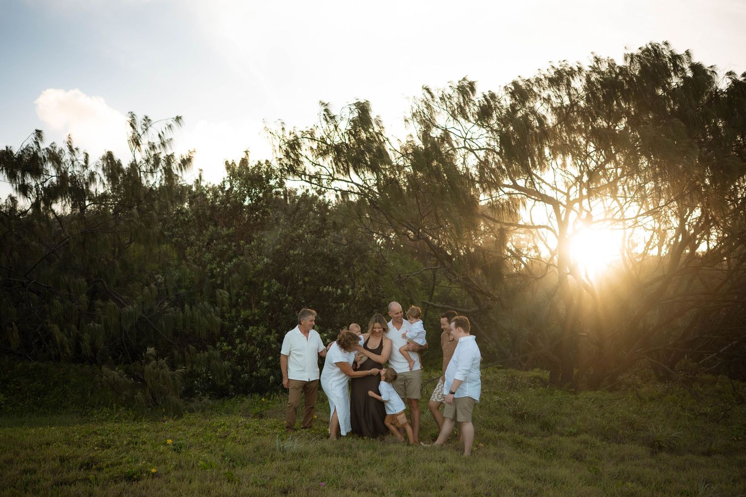 Extended family group gathered together in golden sunset light beside windswept trees in an open field.