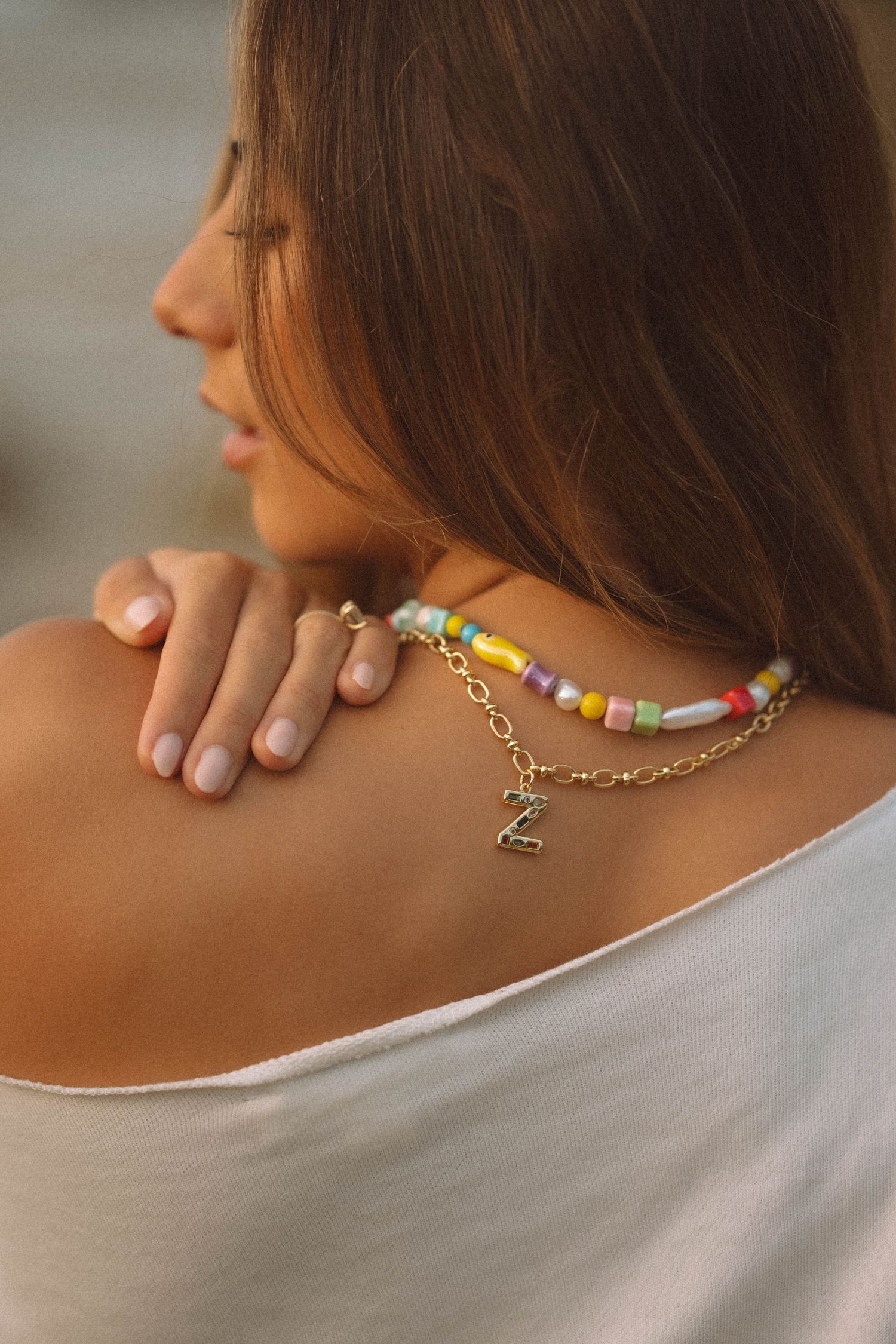 Close-up of colorful beaded necklace with gold letter Z charm on womans shoulder.