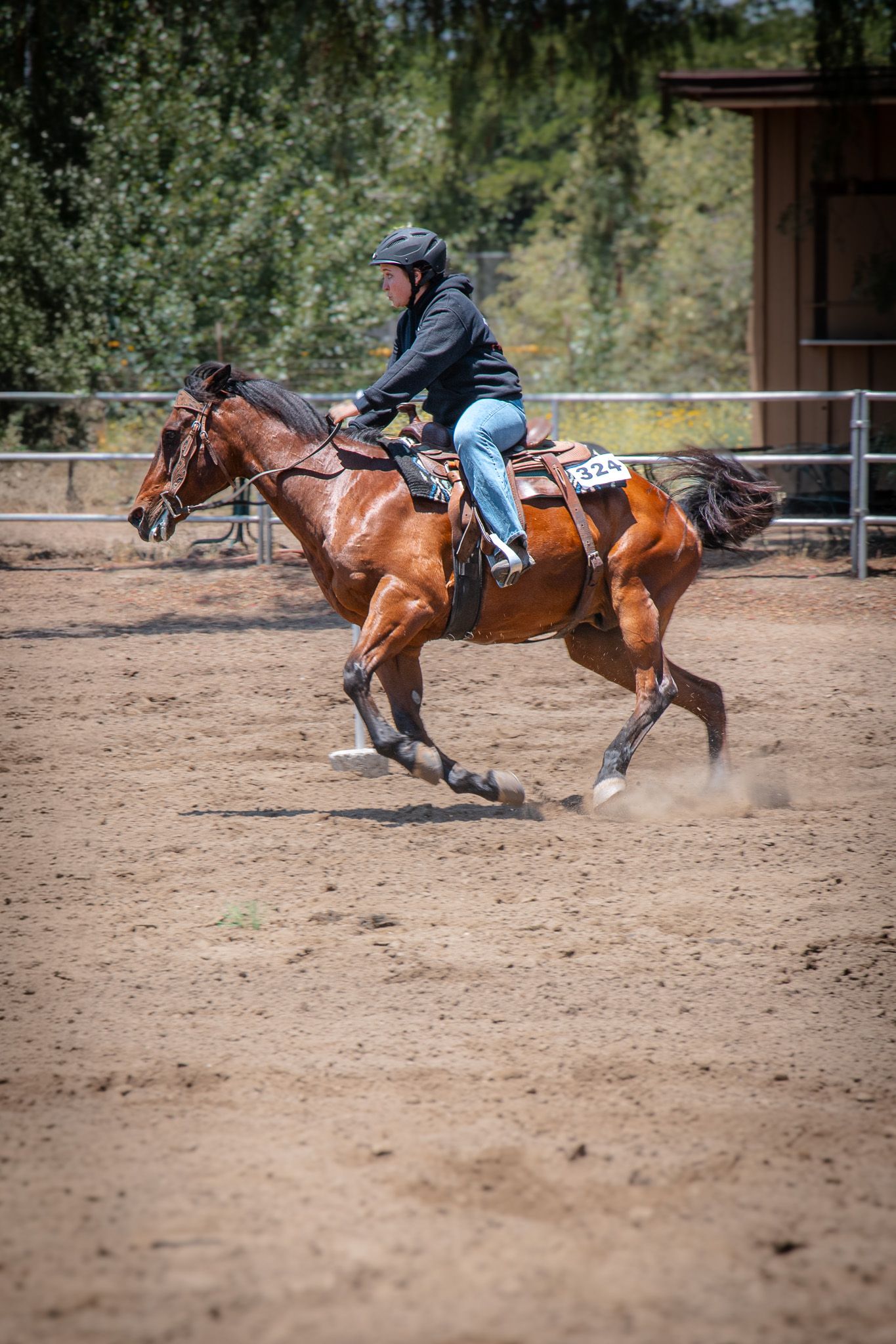 A rider in a helmet races a chestnut horse at full gallop across a sandy arena during an equestrian competition.