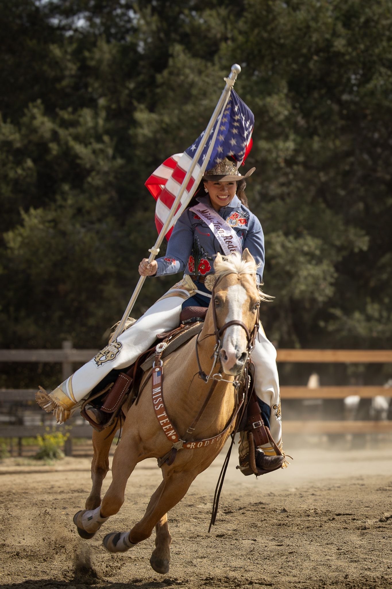Cowgirl riding palomino horse carrying American flag at rodeo competition in Western attire.