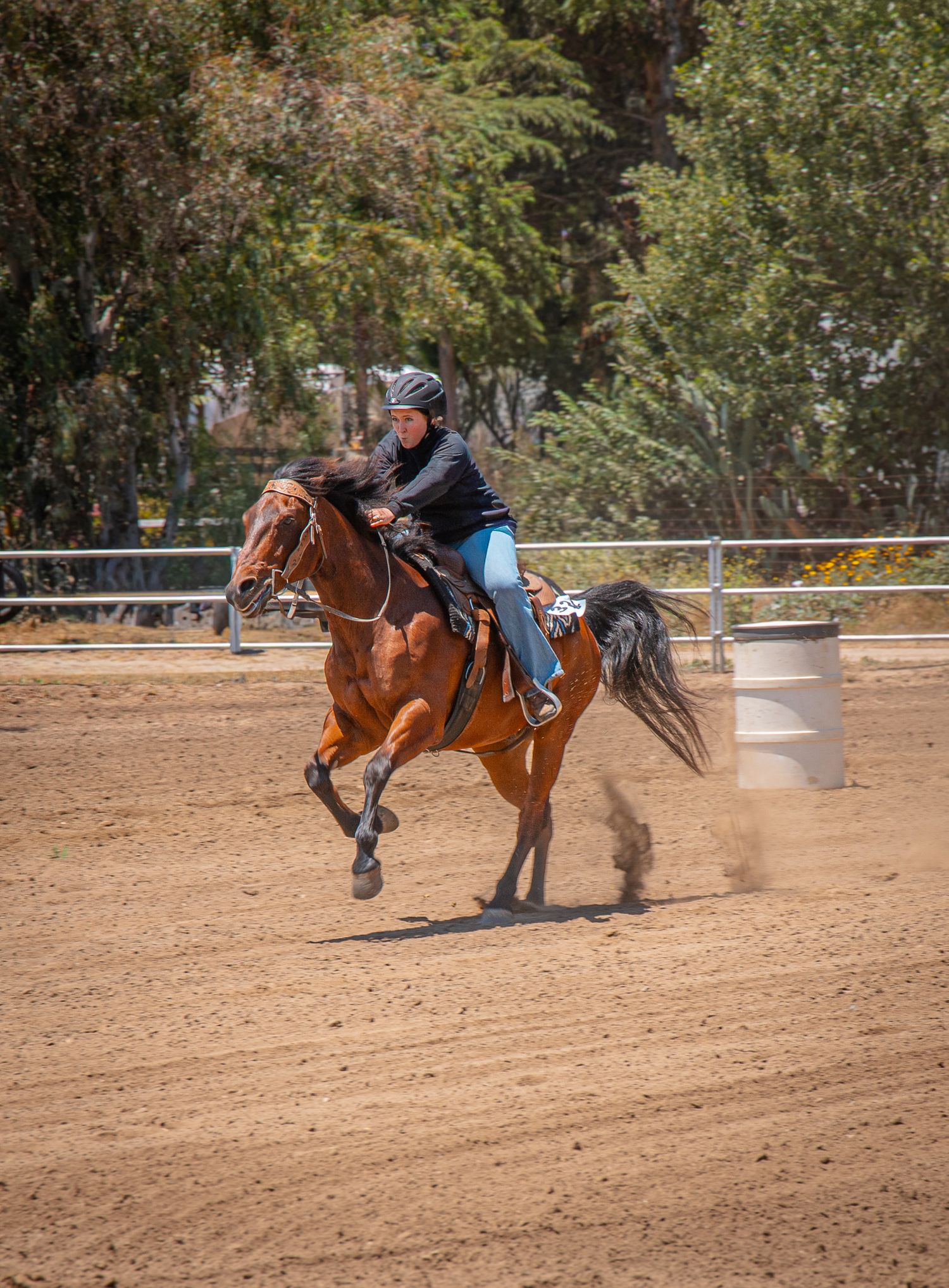 Rider on a chestnut horse galloping around a barrel in a sandy arena competition.
