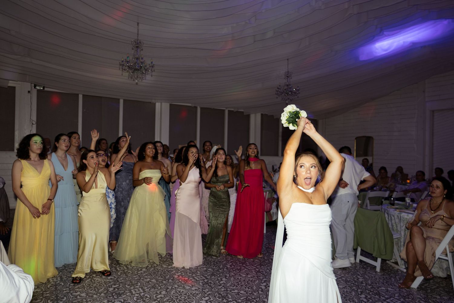 Bride tossing bouquet to excited guests at wedding reception in elegant ballroom.