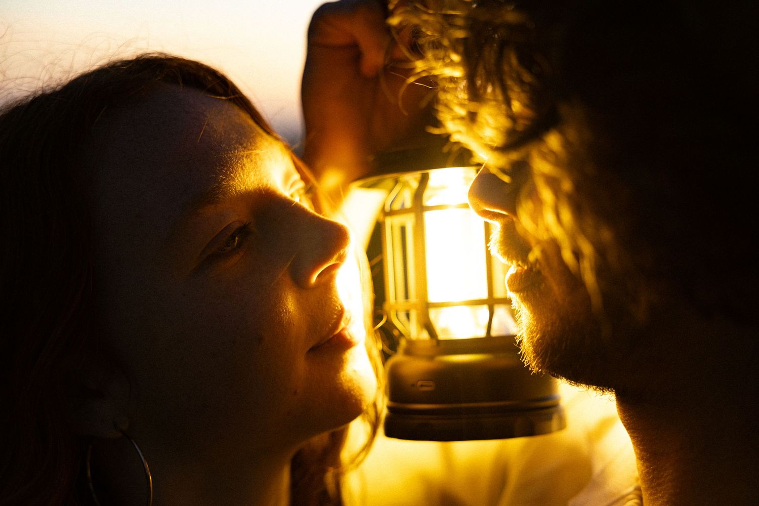 Woman gazing at a glowing vintage lantern in warm golden light, creating a dramatic and mystical atmosphere.
