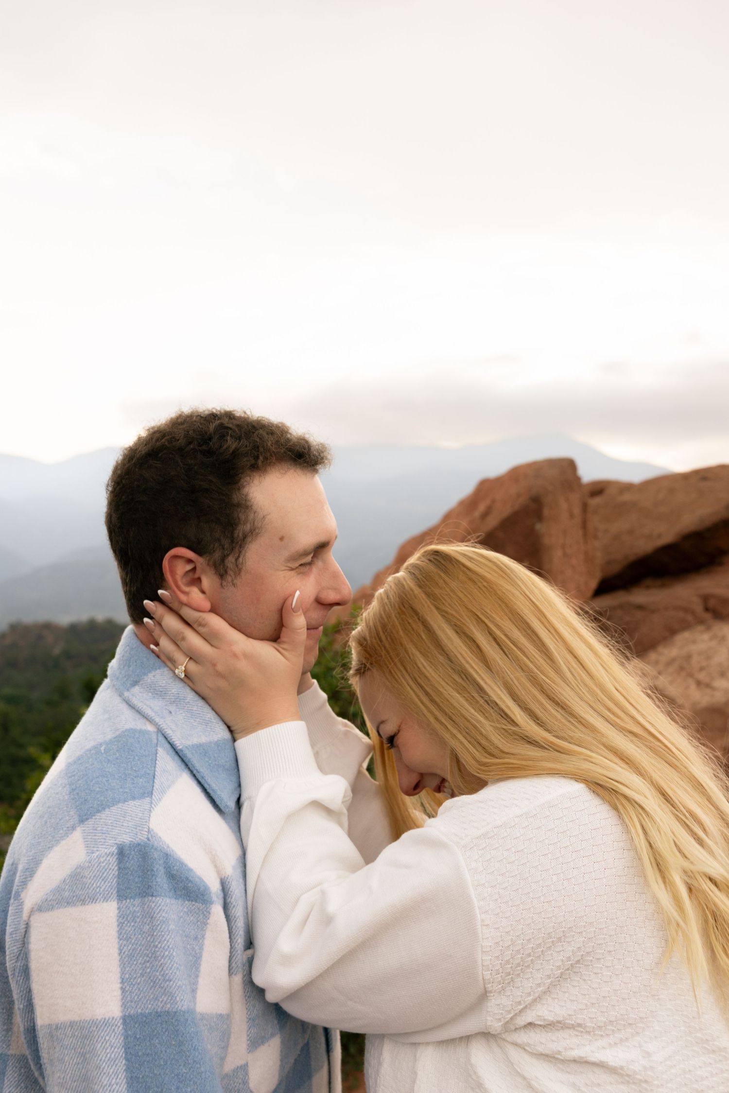 Couple sharing a tender moment outdoors with red rocks and mountains in the background.