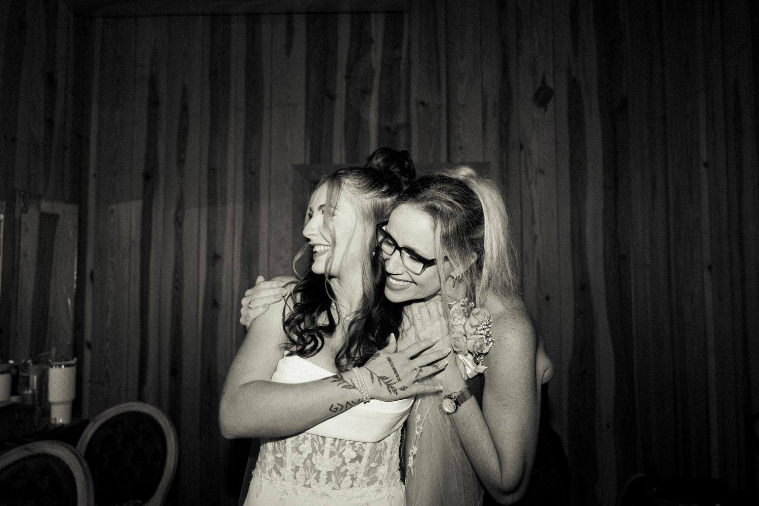 Two women sharing a joyful hug and laughing together in a black and white photo at an indoor event.