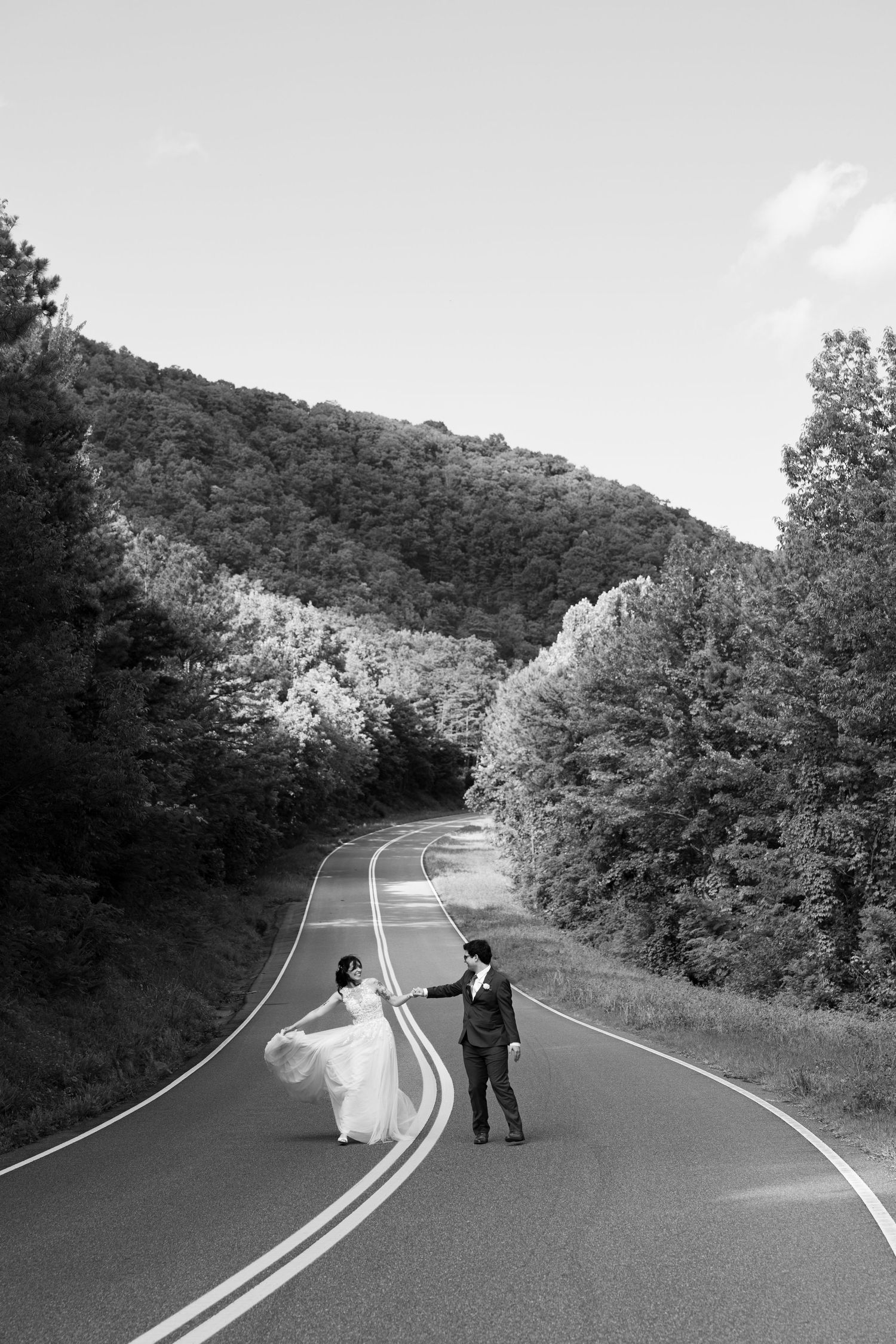Black and white photo of bride and groom dancing on winding mountain road.