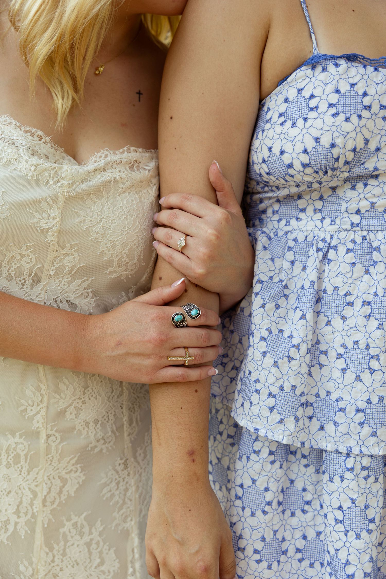 Close-up of two women's hands adorned with gold and turquoise rings, wearing lace and floral dresses.