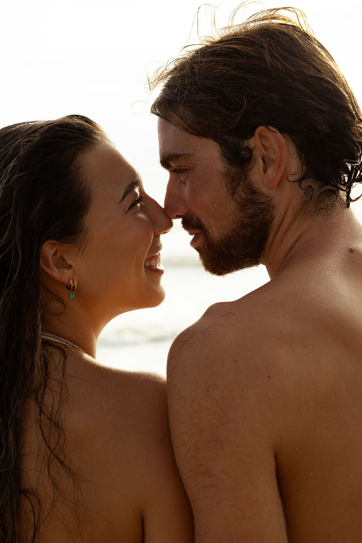 Romantic couple sharing an intimate moment at the beach, smiling and touching noses in warm golden sunlight.