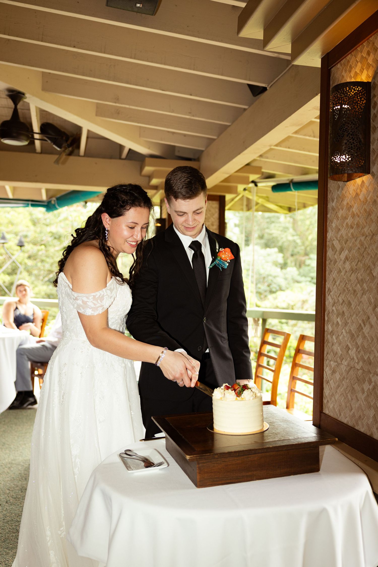 Bride and groom cutting their white wedding cake together at a decorated table in an elegant venue.