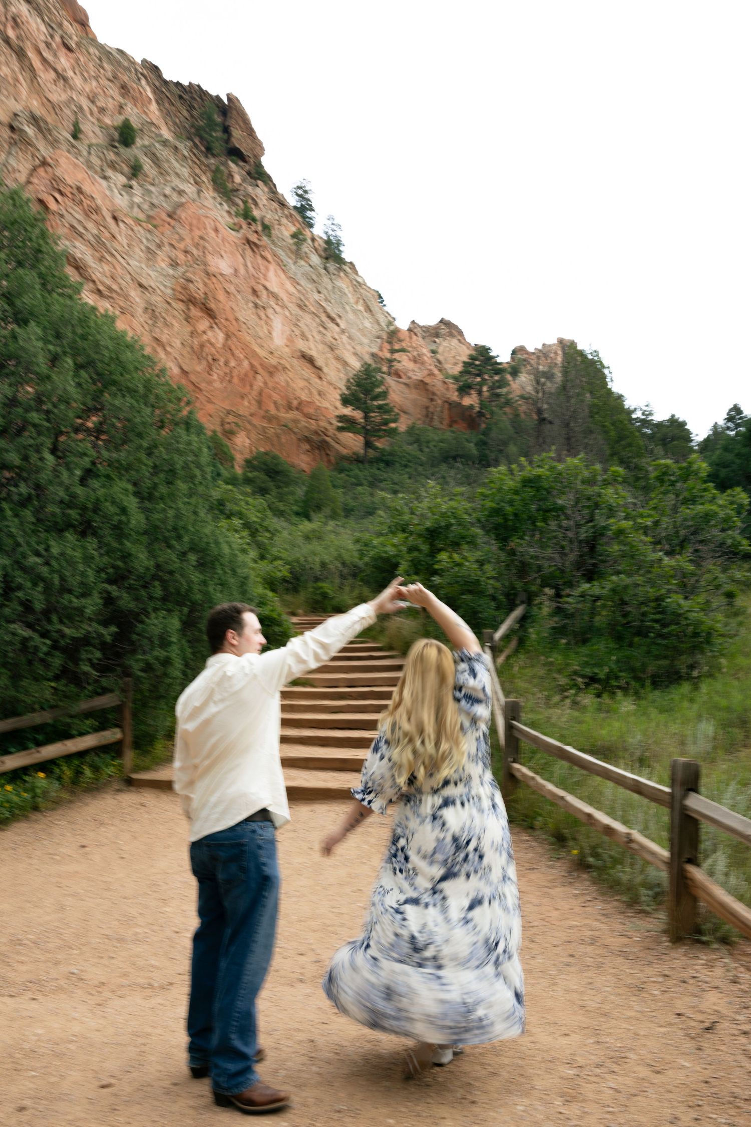 Couple dancing on a scenic red rock trail at Garden of the Gods, Colorado, woman in flowing blue floral dress.