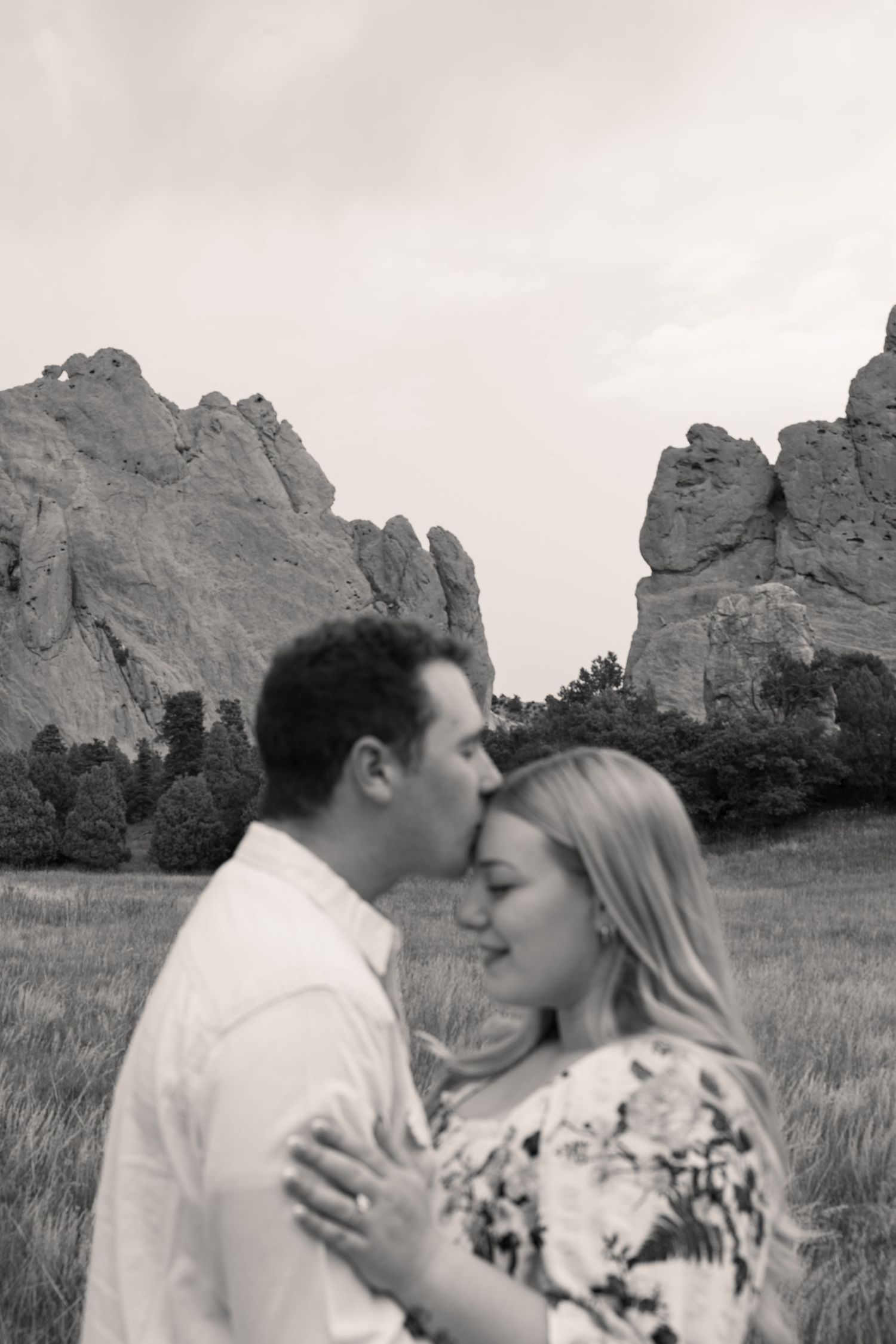 Black and white photo of a couple sharing a tender kiss in front of dramatic rock formations at Garden of the Gods.