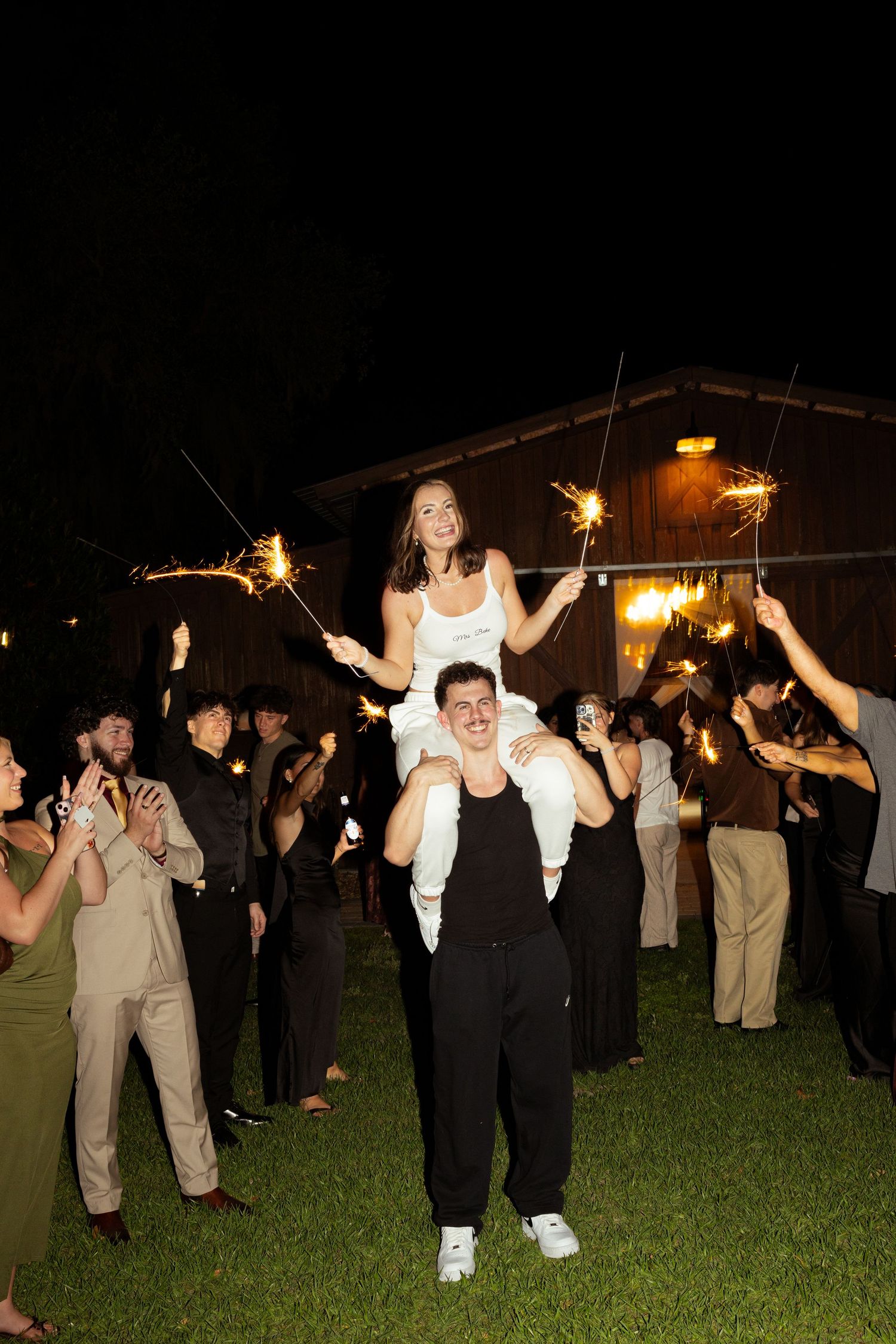 Bride on grooms shoulders during sparkler wedding sendoff celebration at night.