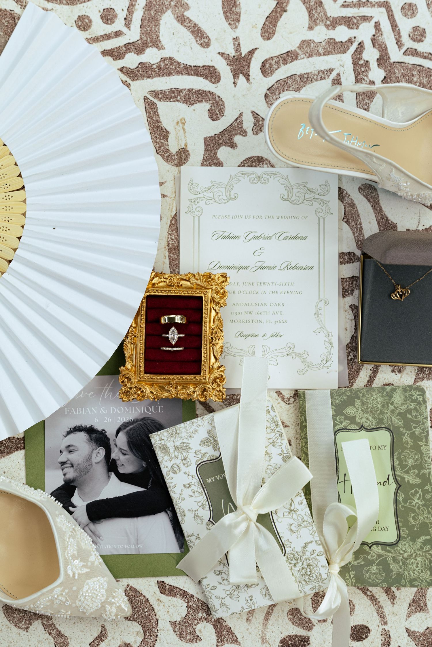 Elegant wedding flat lay with invitation, rings, fan, heels, and floral accessories on decorative background.