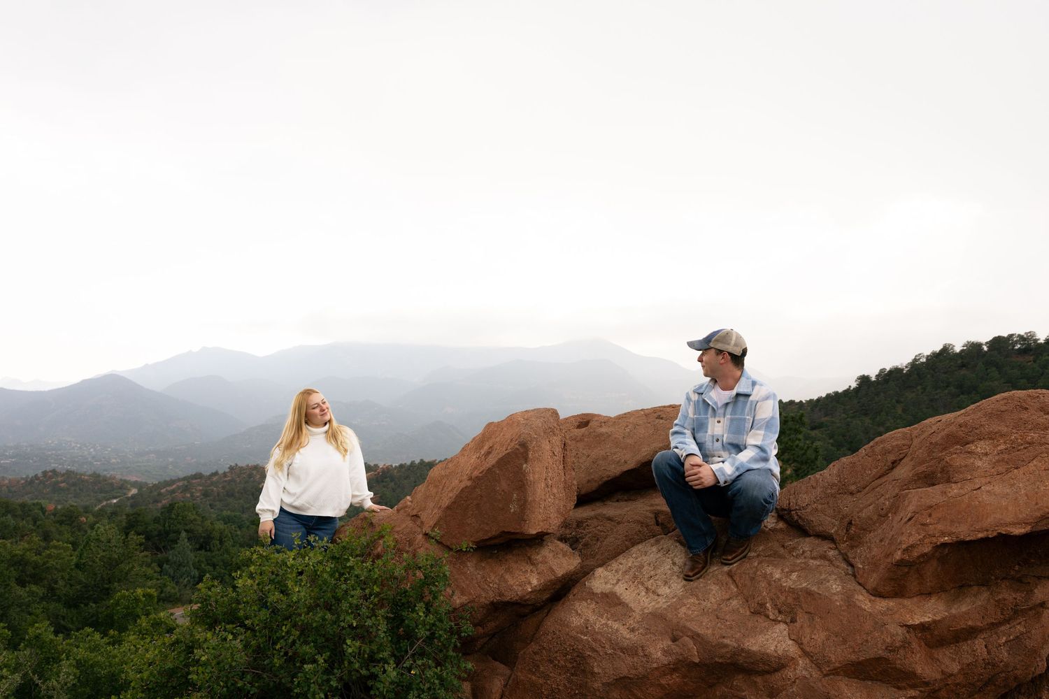 Couple sitting on red rocks at Garden of the Gods with mountain views in background.