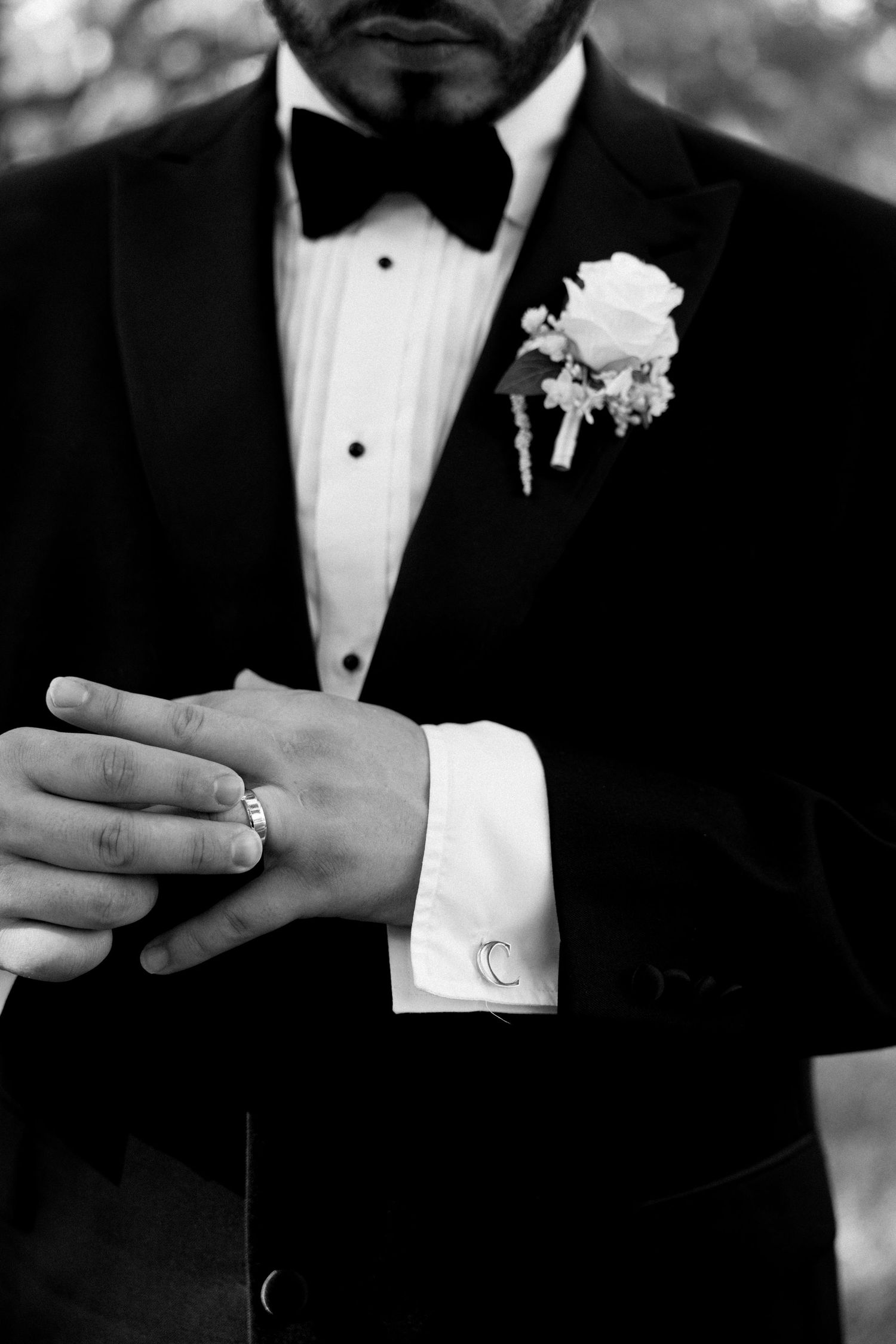 Black and white photo of a groom in a tuxedo with boutonniere, adjusting his cufflinks on his wedding day.