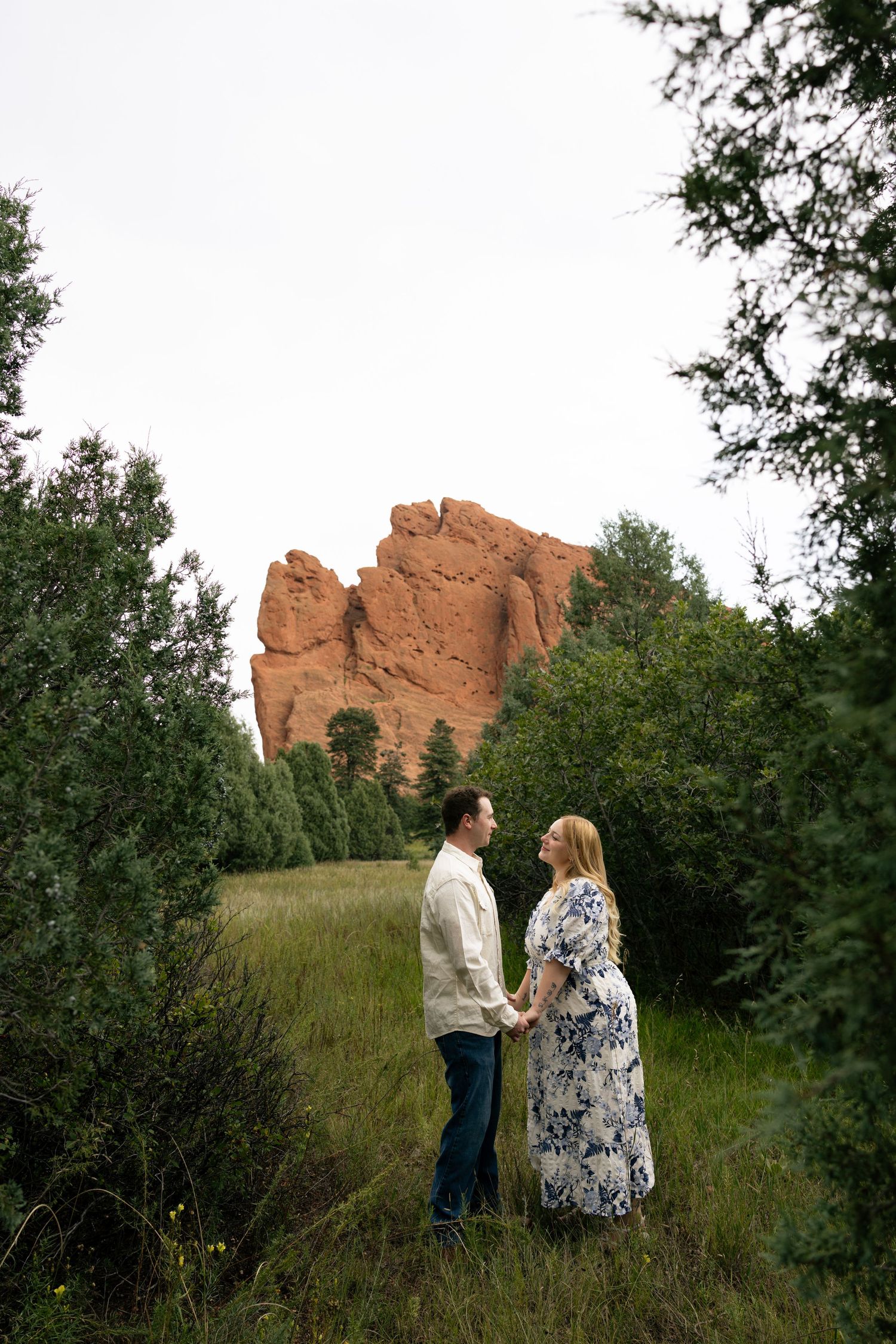 Couple holds hands in a green meadow with red rock formations at Garden of the Gods, Colorado.