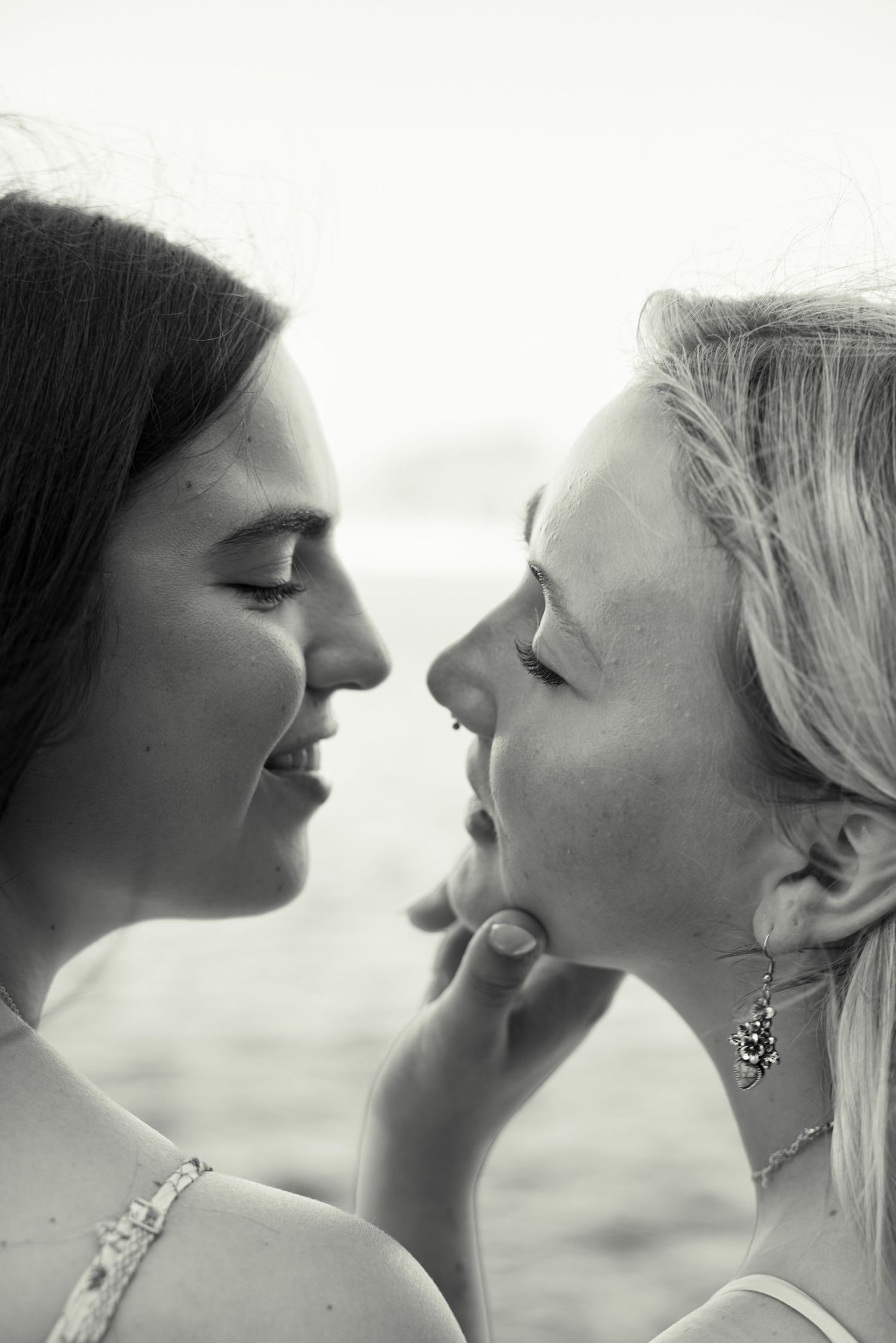 Black and white photo of two smiling women facing each other closely, one touching the others chin tenderly.