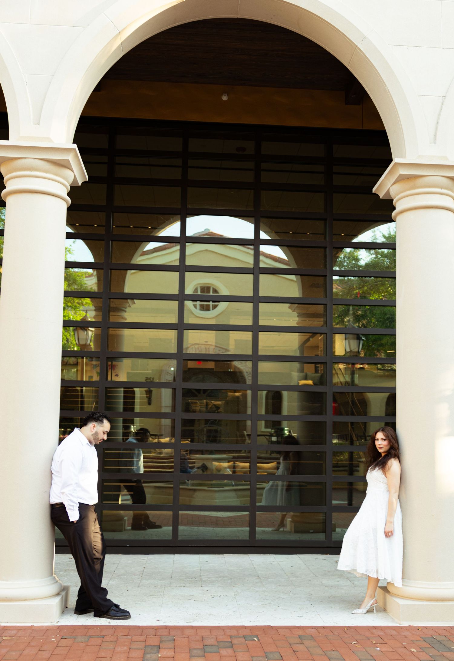 Couple posing apart under elegant arched entrance with large glass doors and white columns at upscale venue.