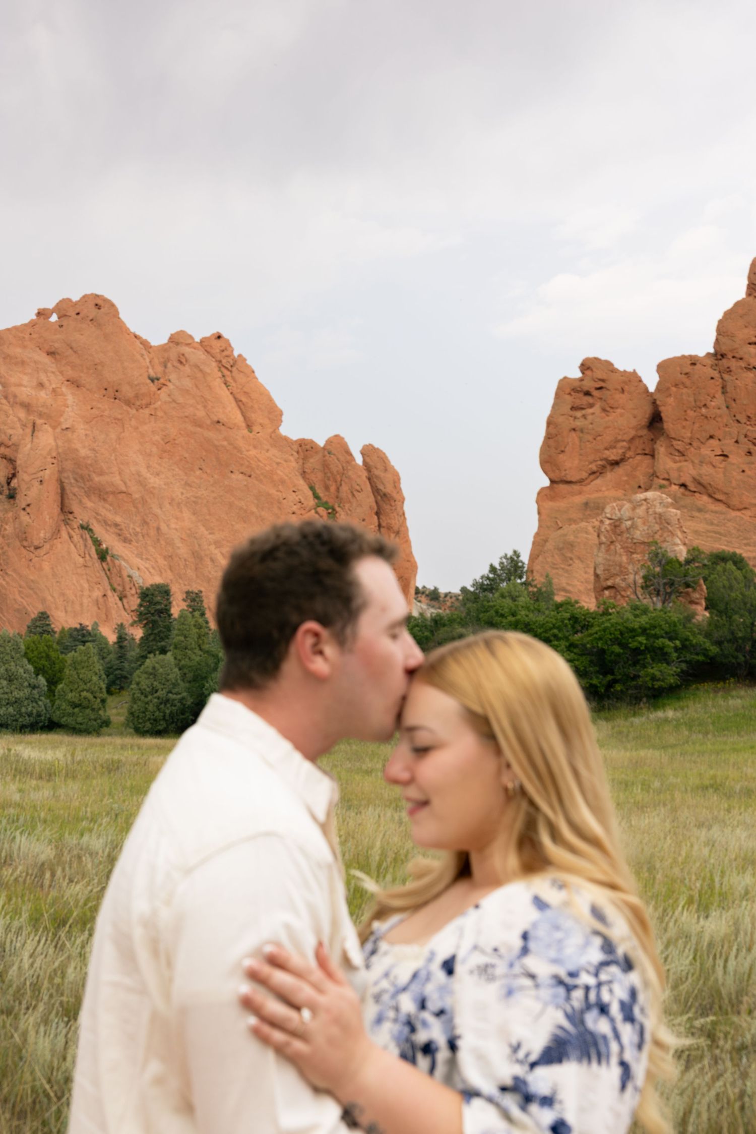 Couple sharing a tender kiss with stunning red rock formations at Garden of the Gods in background.