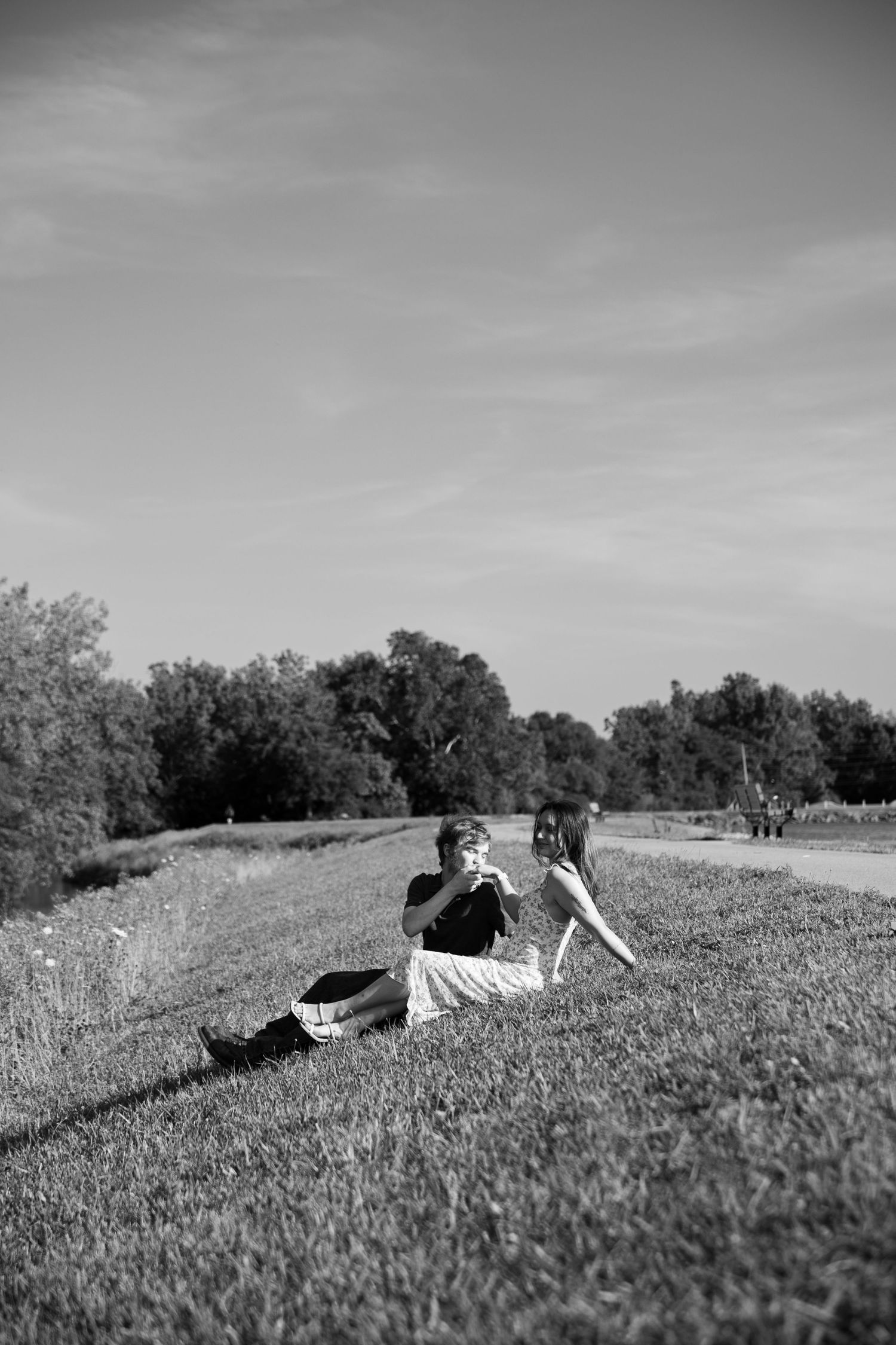 Black and white photo of a couple sitting on a grassy hillside talking during an outdoor engagement session.