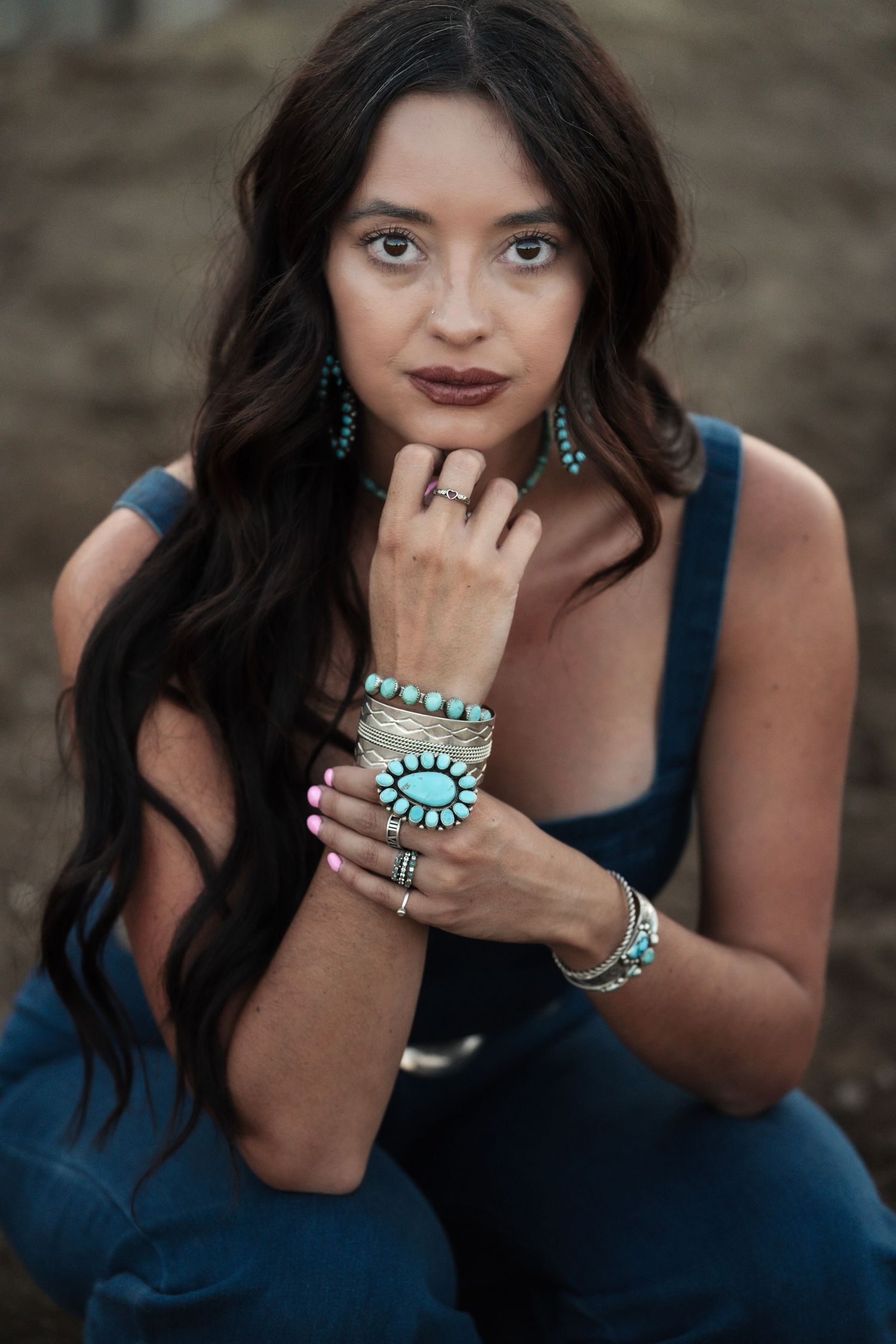 Girl wearing turquoise jewelry sitting on the ground in a western lifestyle photoshoot with rustic elements.