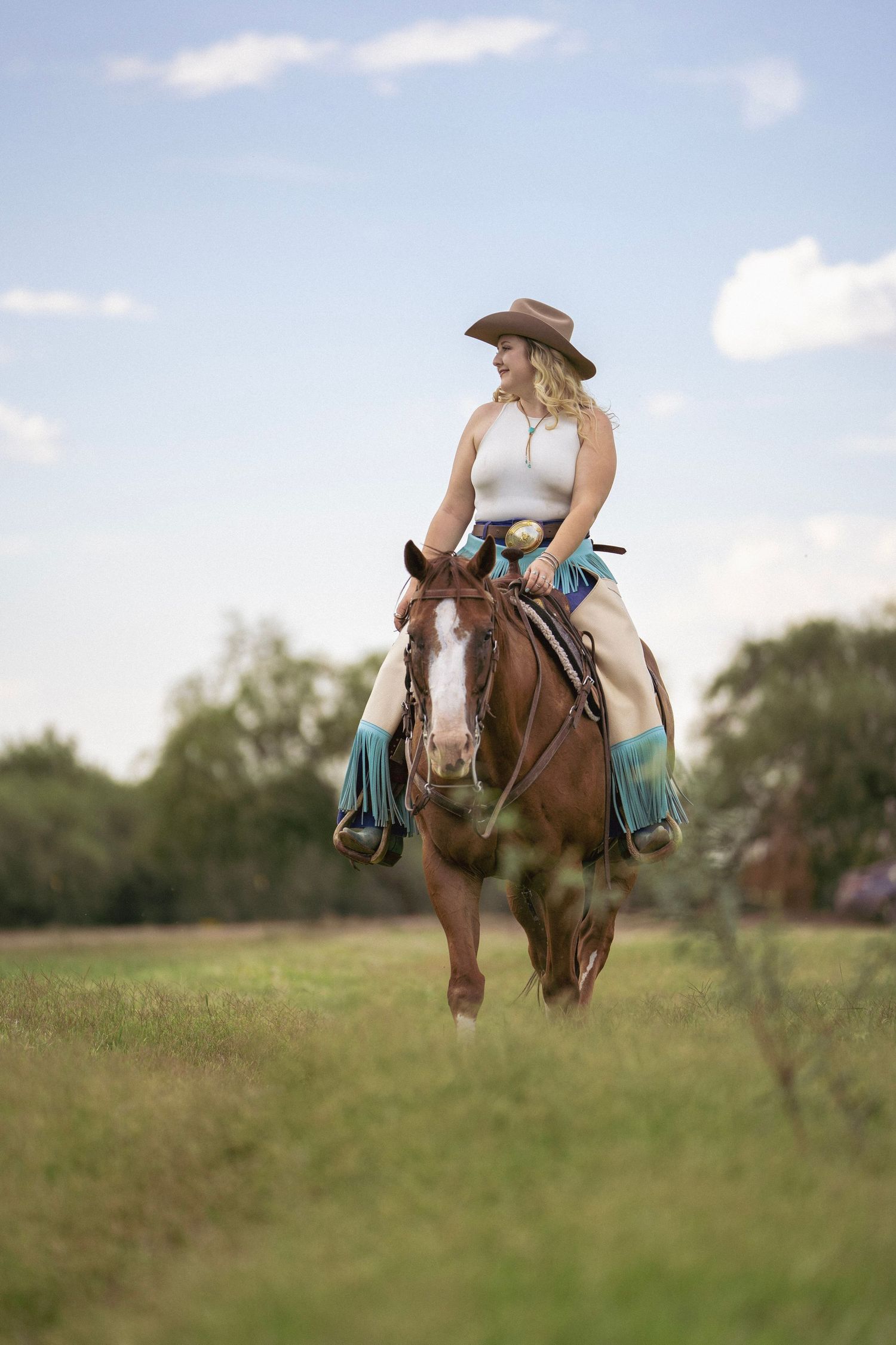 Cowgirl riding her horse through green grass with mountains in the background during a western photoshoot.