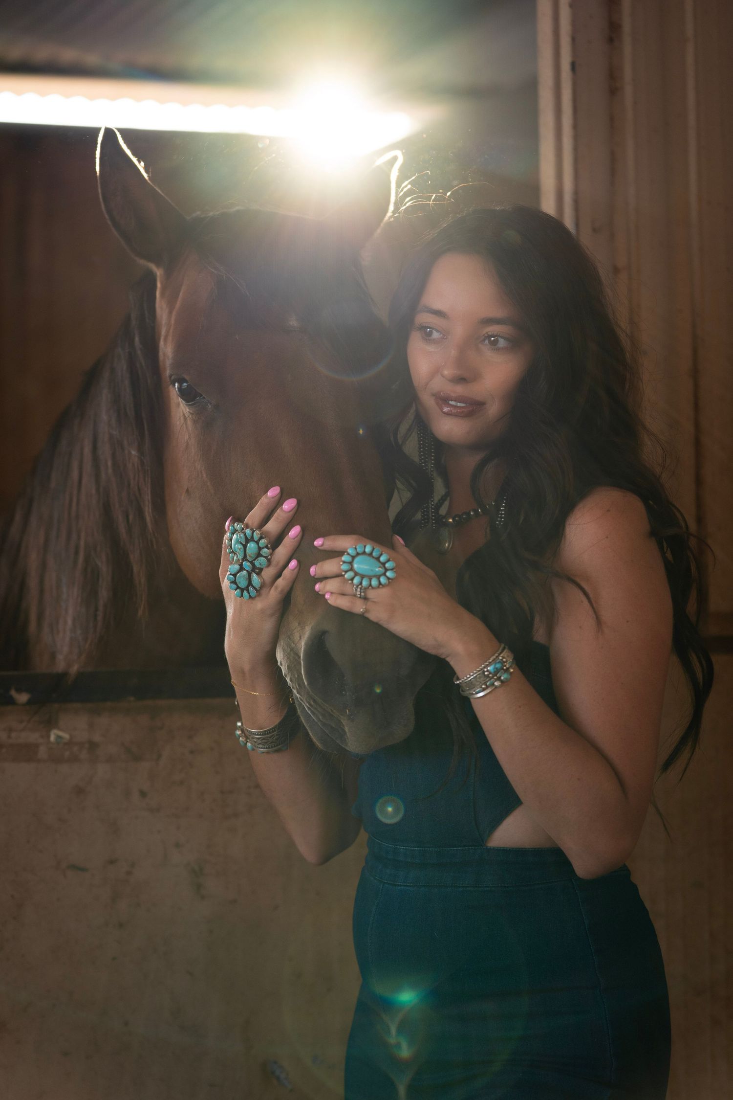 Girl leaning against a horse wearing a denim outfit and layered turquoise jewelry during a western lifestyle photoshoot.