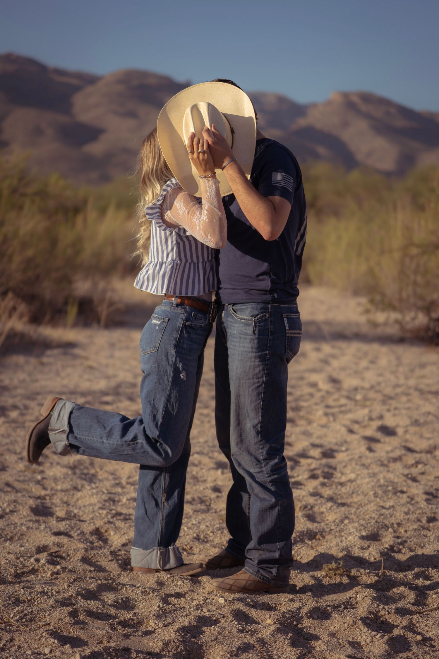 Couple sharing a kiss behind a cowboy hat during a boho western photoshoot in the Arizona desert.