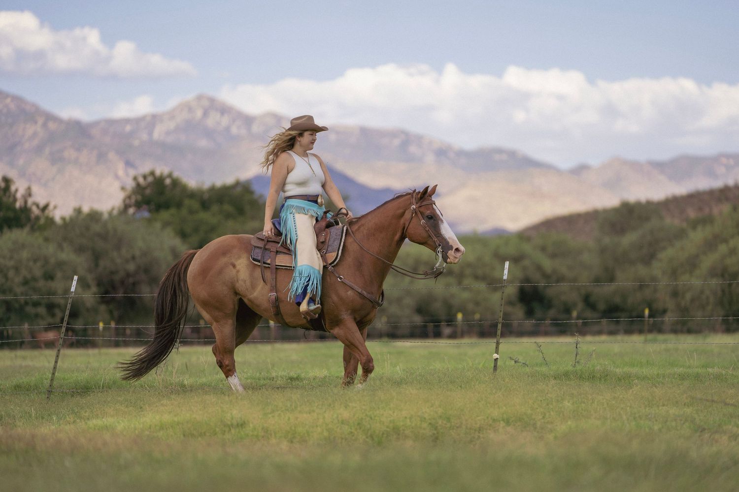 Cowgirl riding her horse through green grass with mountains in the background during a western photoshoot.