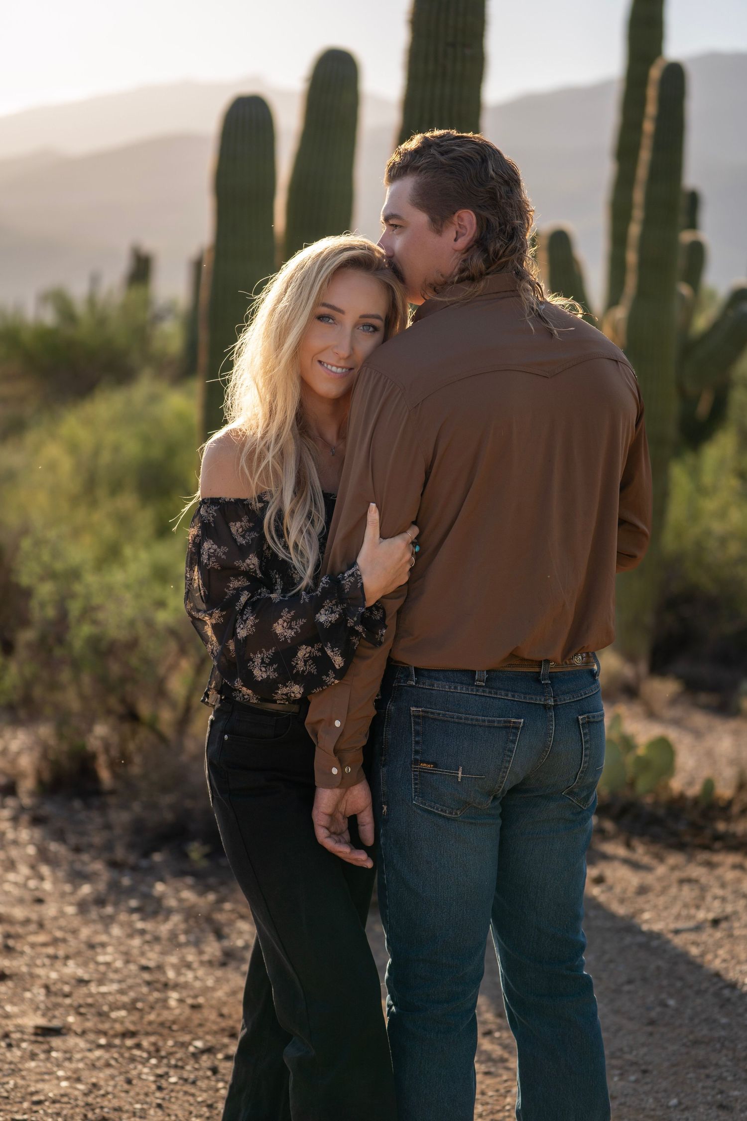 Couple holding each other closely during a western photoshoot in the Arizona desert at sunset.