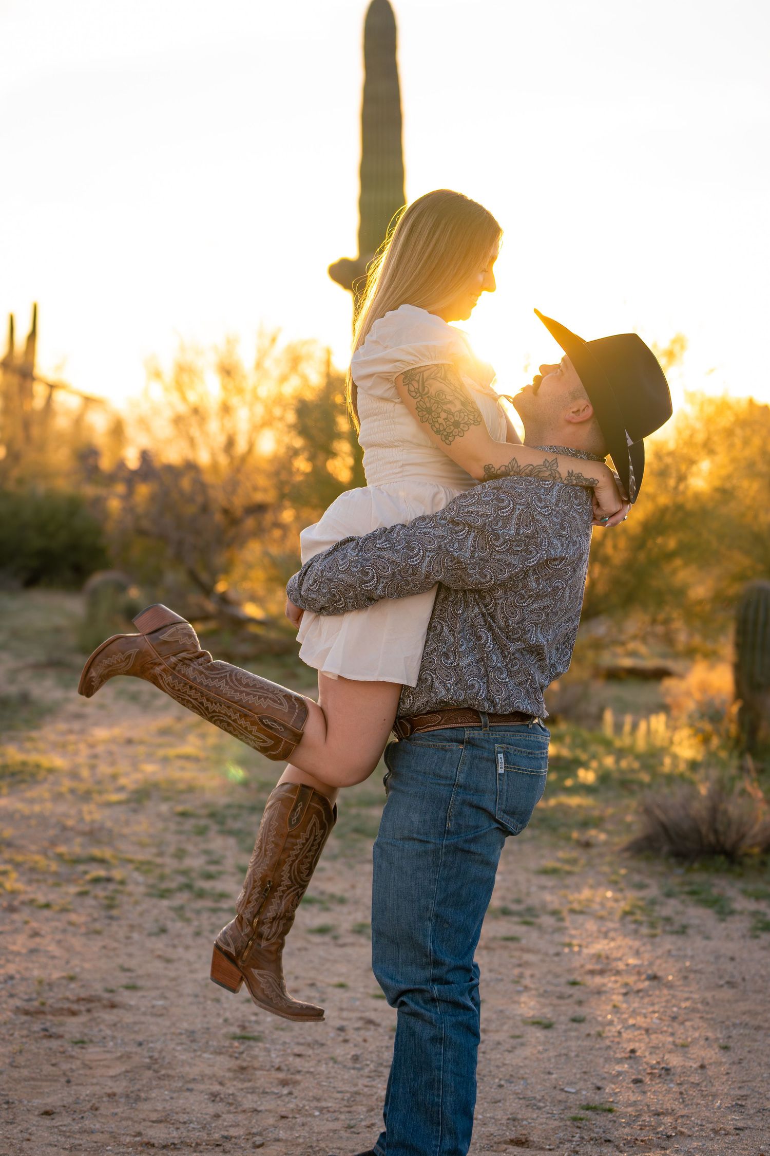 Western engagement photo in Arizona desert with cowboy lifting cowgirl at golden hour sunset