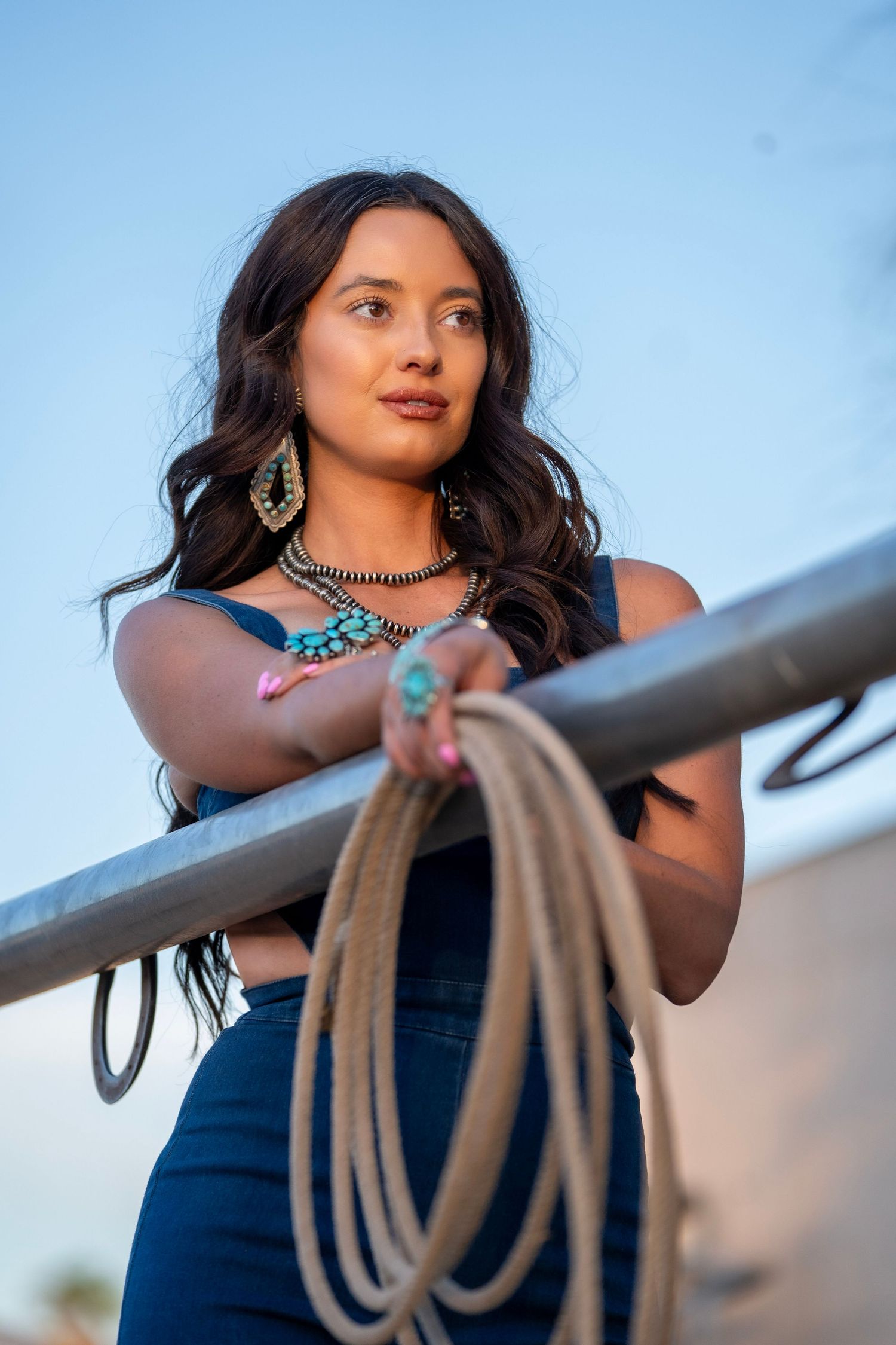 Girl wearing turquoise jewelry holding a rope in a western lifestyle photoshoot with rustic elements.