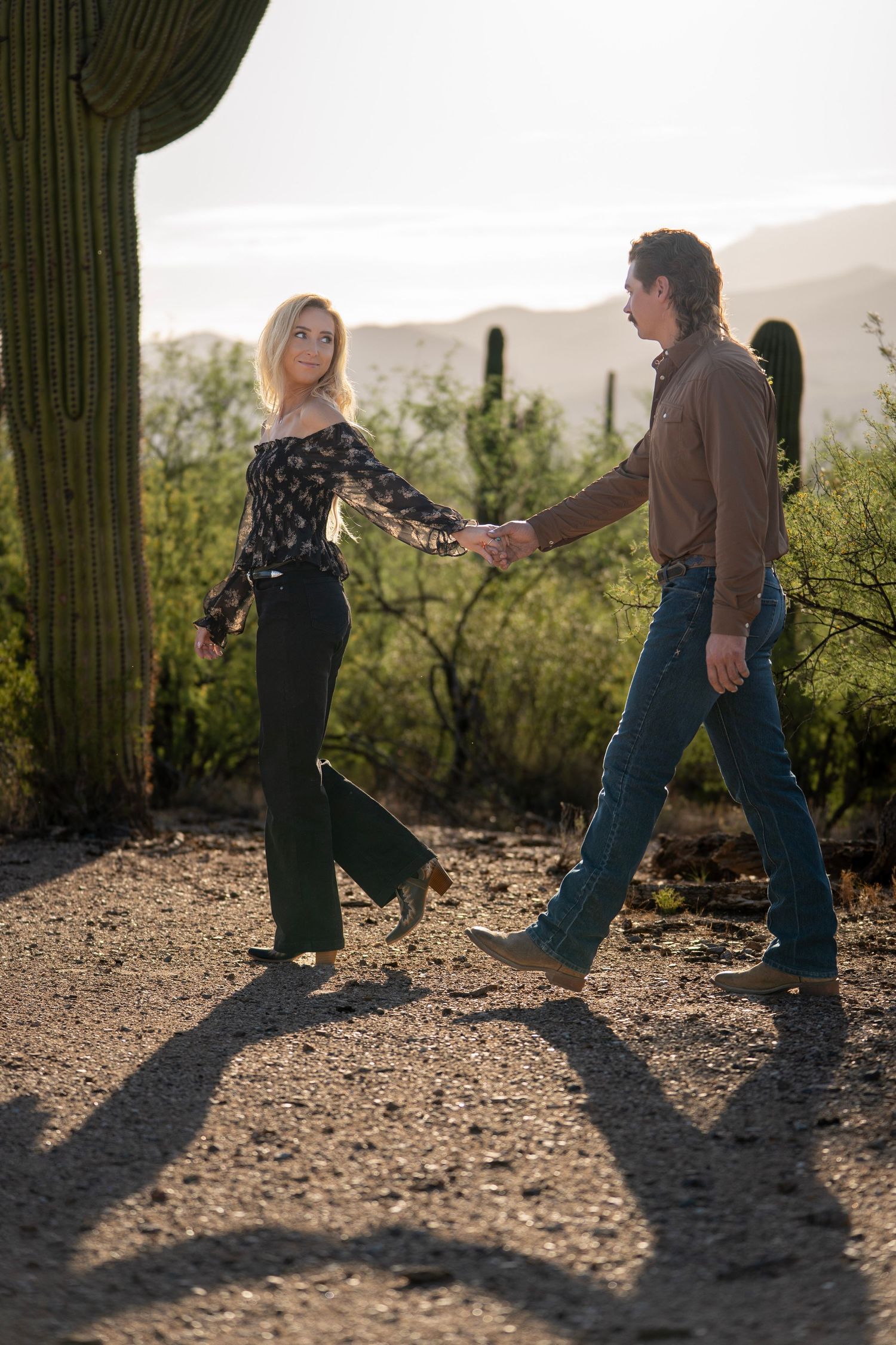 Couple walking hand in hand through the desert during golden hour in Tucson, Arizona.