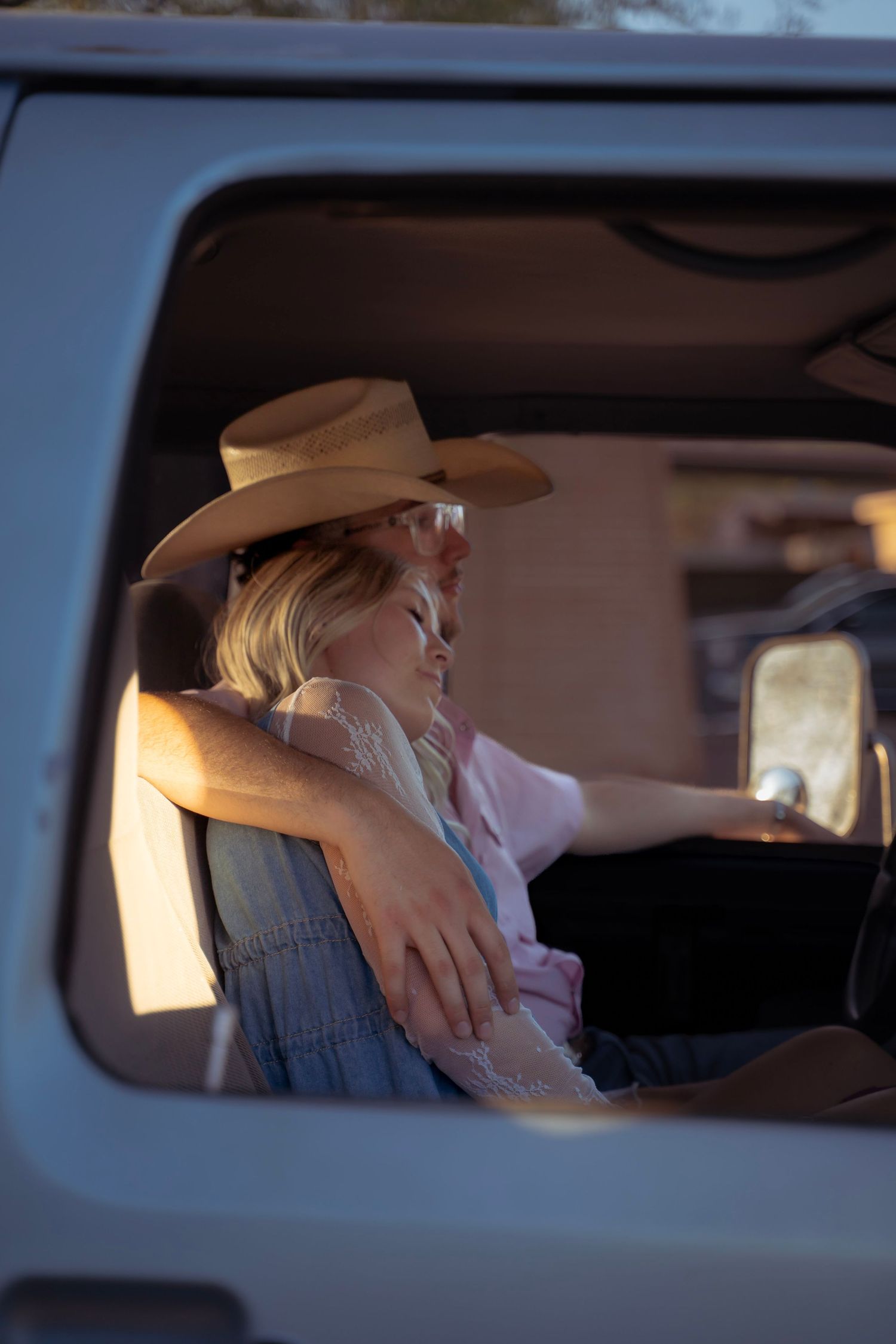 Couple dressed in western outfits sitting close together in an old pickup truck during a desert photoshoot.
