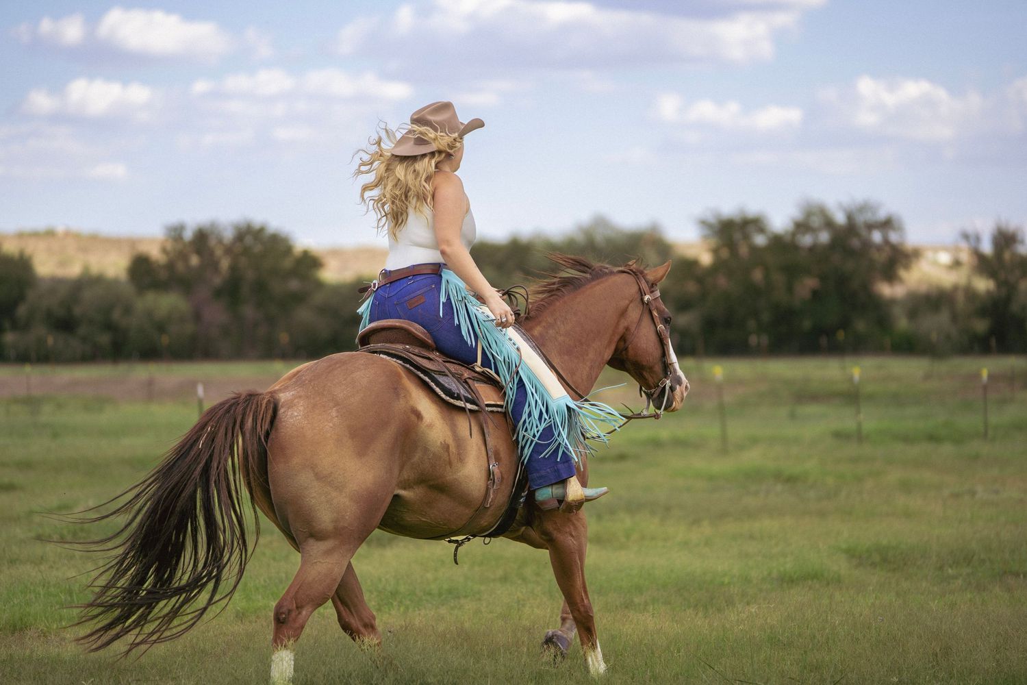 Cowgirl riding her horse through green grass with mountains in the background during a western photoshoot.