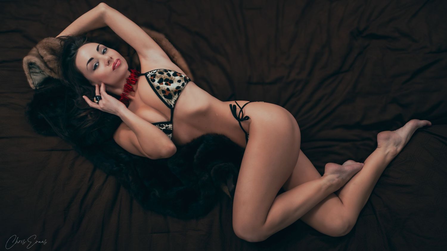 A person in black lingerie poses gracefully on dark bedding in a sensual boudoir photo series.