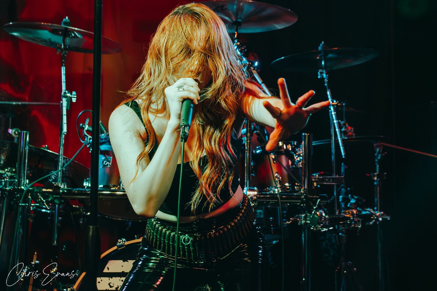 Concert photographer captures performer with flowing hair singing on stage with drum kit in background.