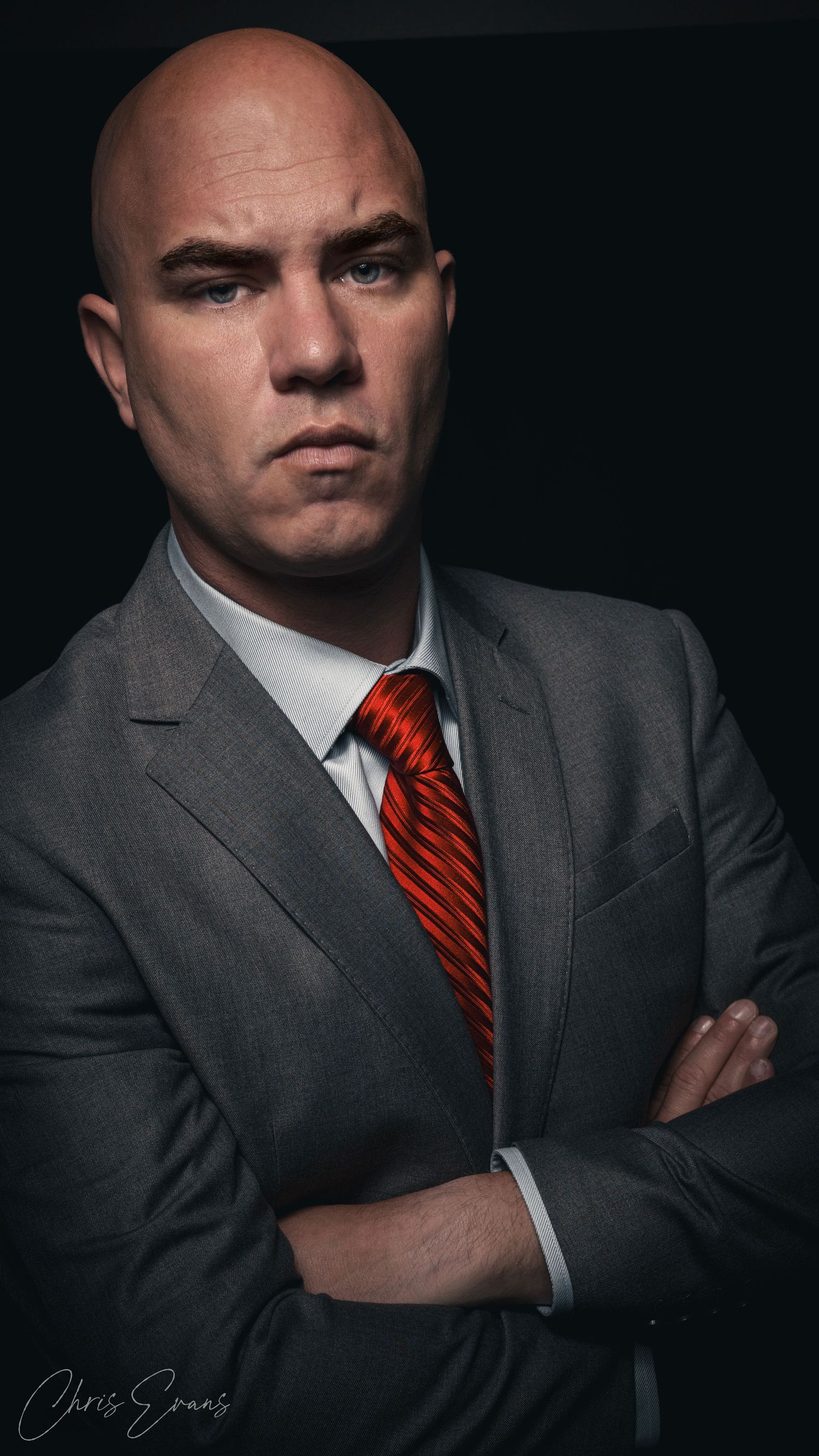 Professional studio portrait of businessman in grey suit and red tie against dark background.