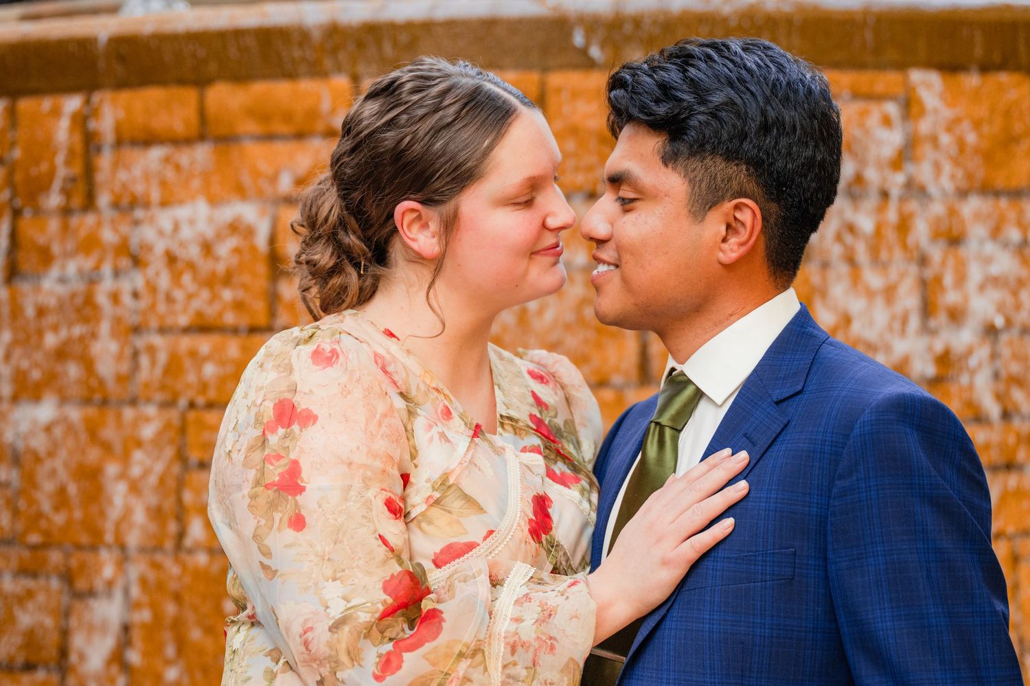 Romantic wedding portraits captured against rustic orange stone wall background.