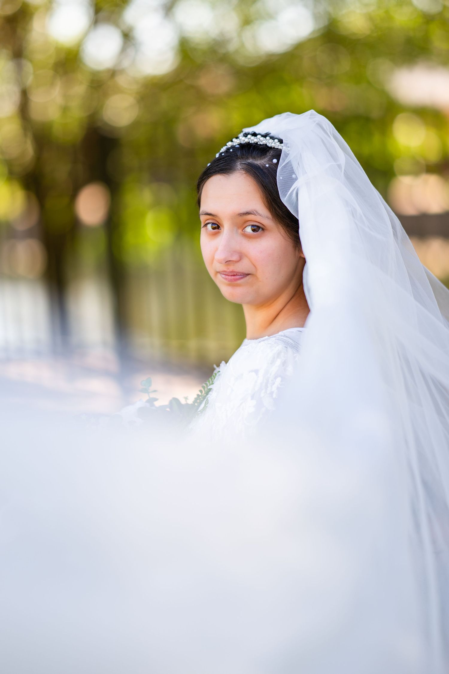 Ethereal bridal portraits with soft focus and flowing white veil against natural outdoor background.